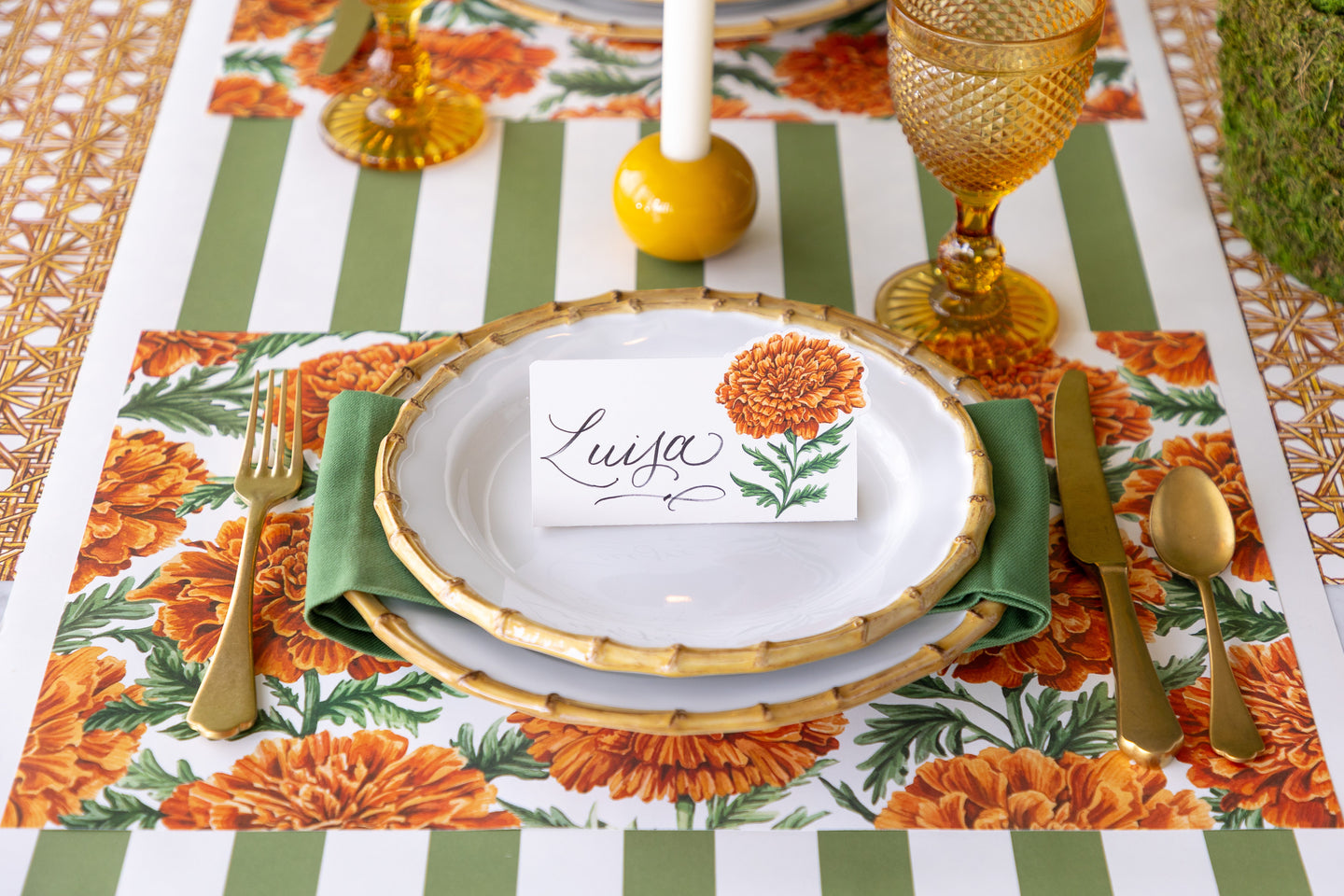 A fall table setting featuring the Marigold Bloom Placemat and bamboo dinnerware with the Marigold Place Card reading "Luisa" atop.