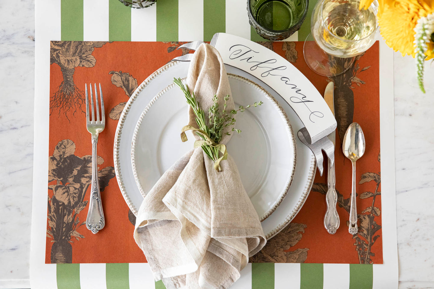 A plate of fresh carrots on a table with a vegetable-themed tablecloth, flanked by cutlery with orange handles.
