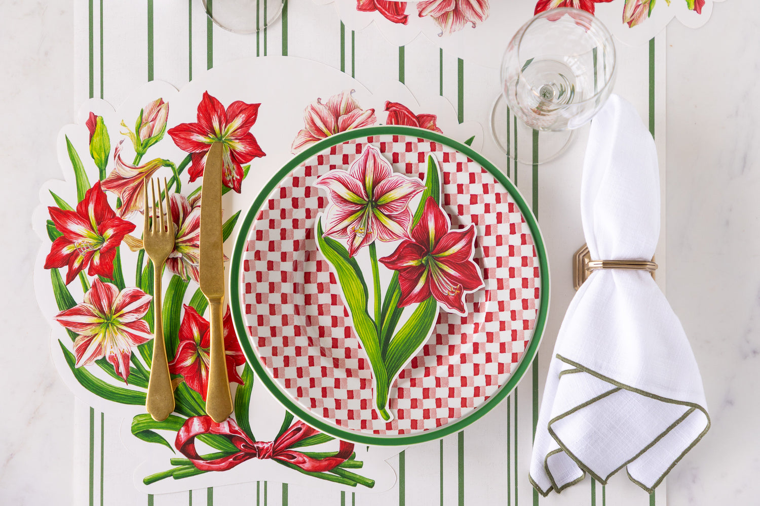 A festive place setting featuring the Die-cut Amaryllis Placemat with Amaryllis Table Accent atop red-and-white checkered plate, a napkin and gold flatware on the Antique Green Striped Runner. 