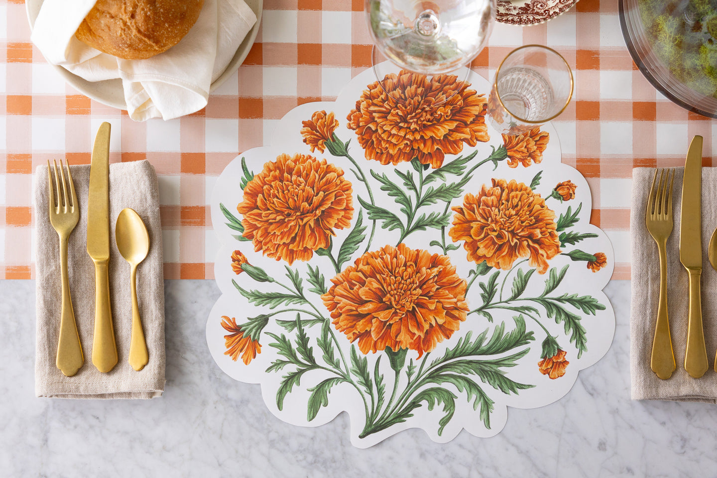 Die-cut Marigold Placemat on a table setting with gold flatware, elegant glassware and a plate of bread on the Orange Painted Check Runner.