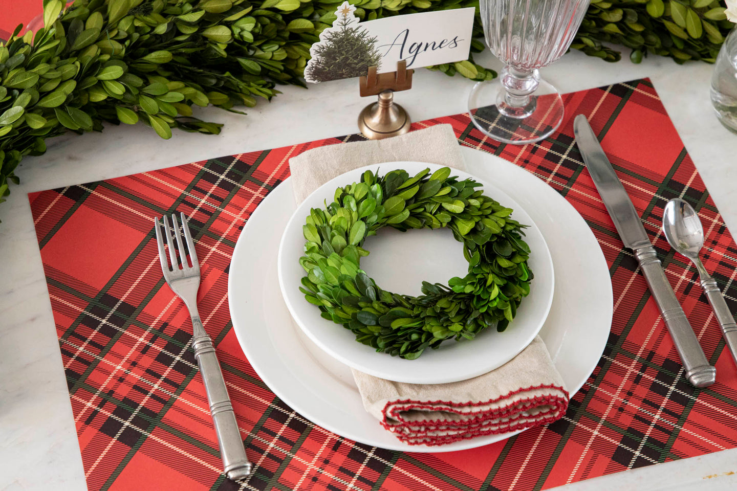 A holiday place setting featuring the Red Plaid Placemat, white dinnerware, a topiary wreath and vintage silverware.