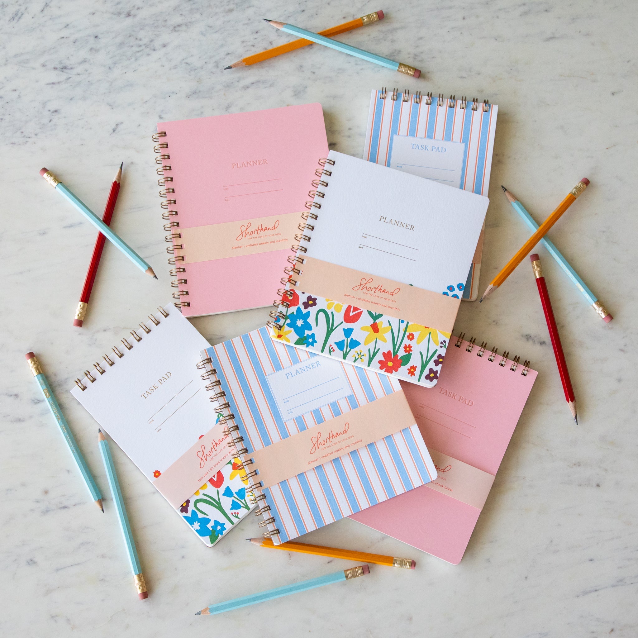Shorthand Press task pads and planners arranged on a table with scattered pencils.