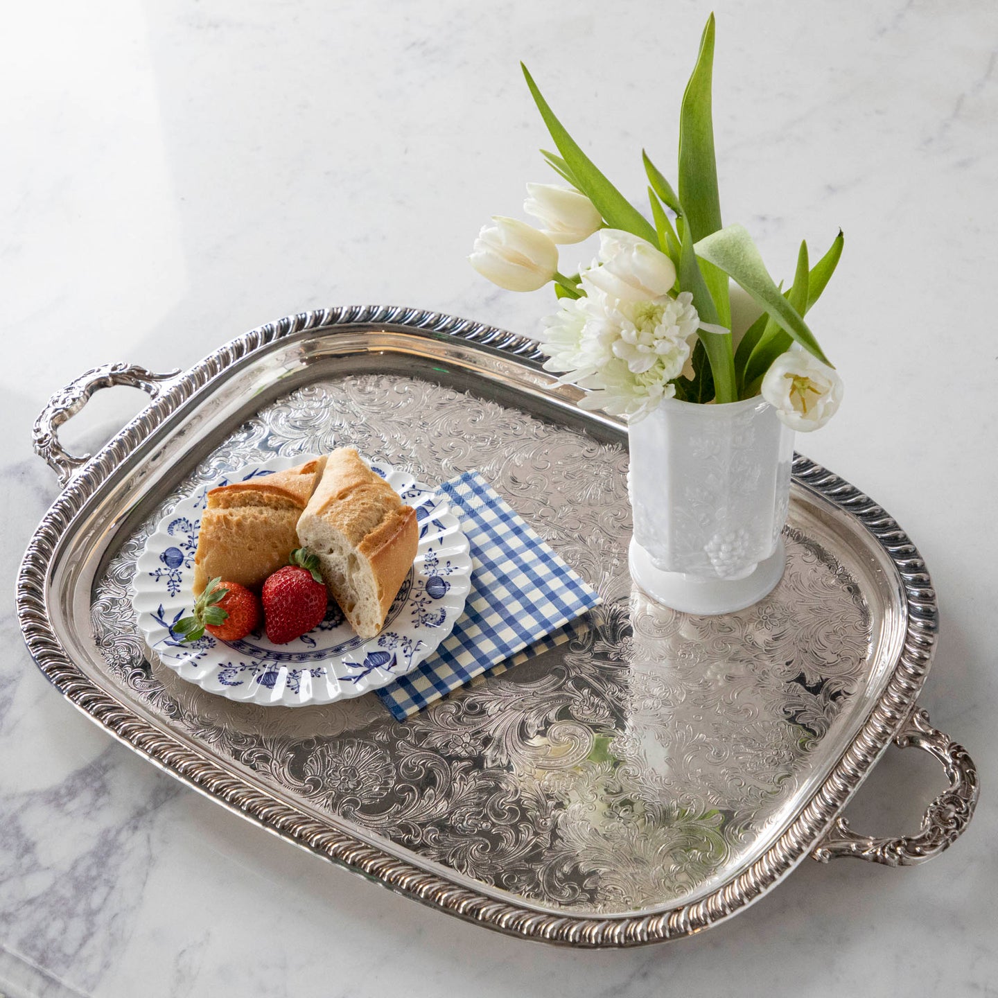 A vintage silver-plate tea tray with a vase of flowers, Blue Painted Check Napkin and plate of bread and strawberries atop.