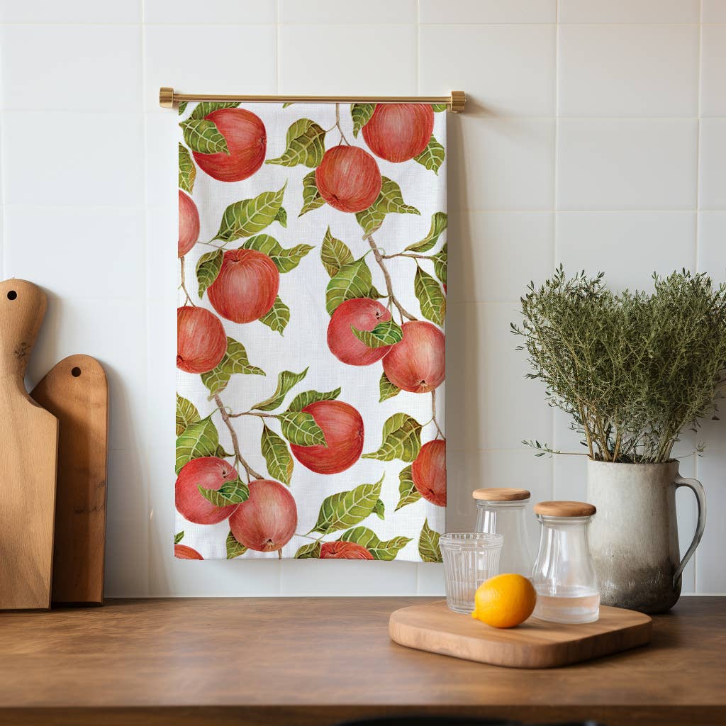 Towel with red apple pattern hanging on a wall above a wooden table with kitchen items.