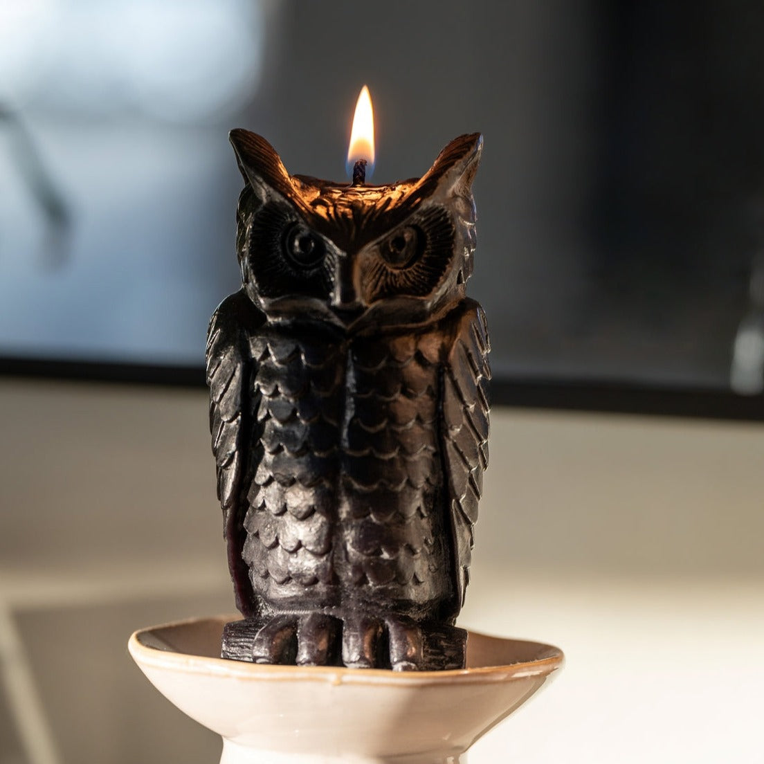 A lit beeswax candle shaped like an owl in spooky black.