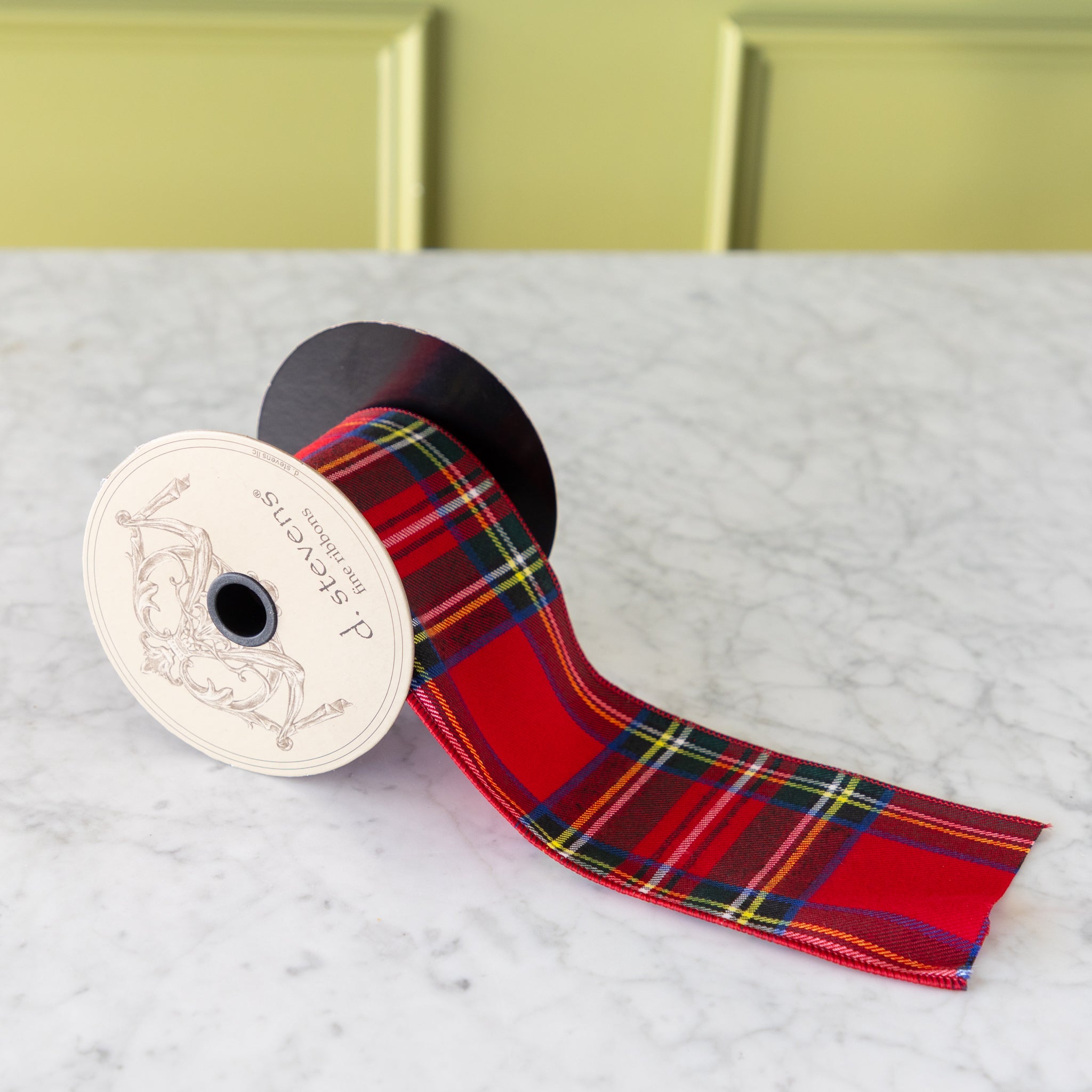 Roll of red plaid ribbon on a marble surface with a green panel background.