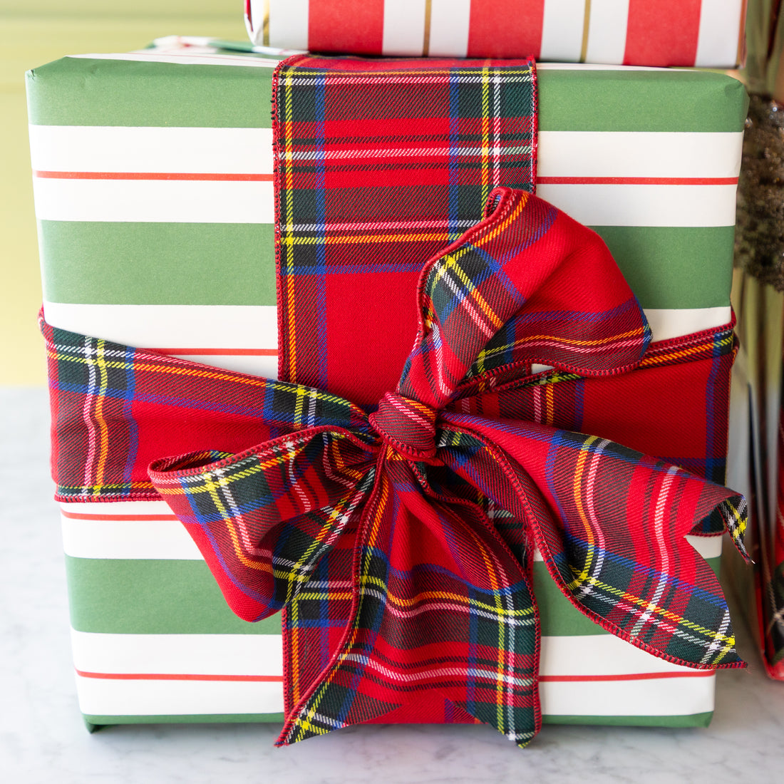 Stack of gift boxes wrapped in red, green, and white stripes with a plaid bow.