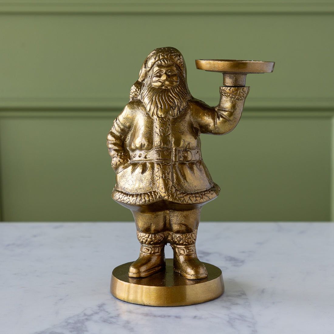 Gold Saint Nick Figurine holding a candle holder on a marble surface with a green wall background.