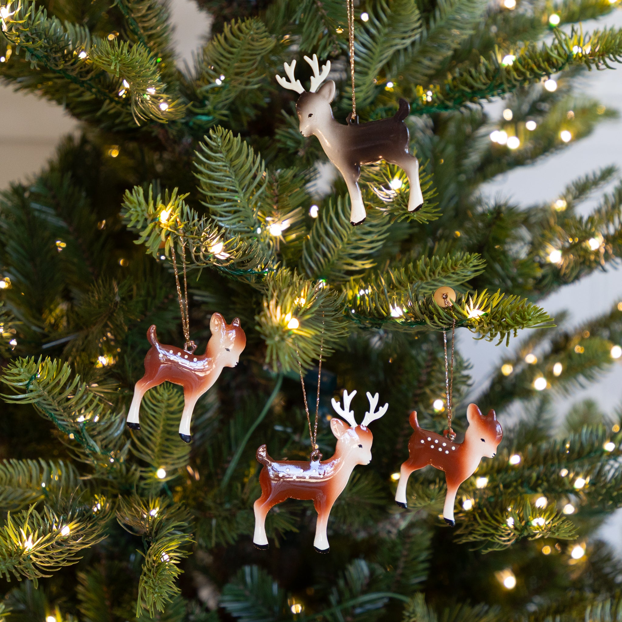Deer-shaped Christmas tree ornaments hanging on a decorated tree with lights.