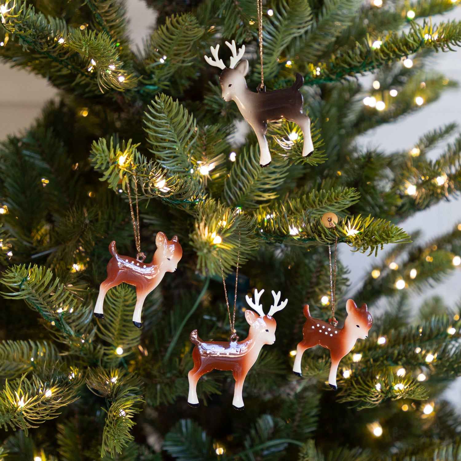 Deer-shaped Christmas tree ornaments hanging on a decorated tree with lights.