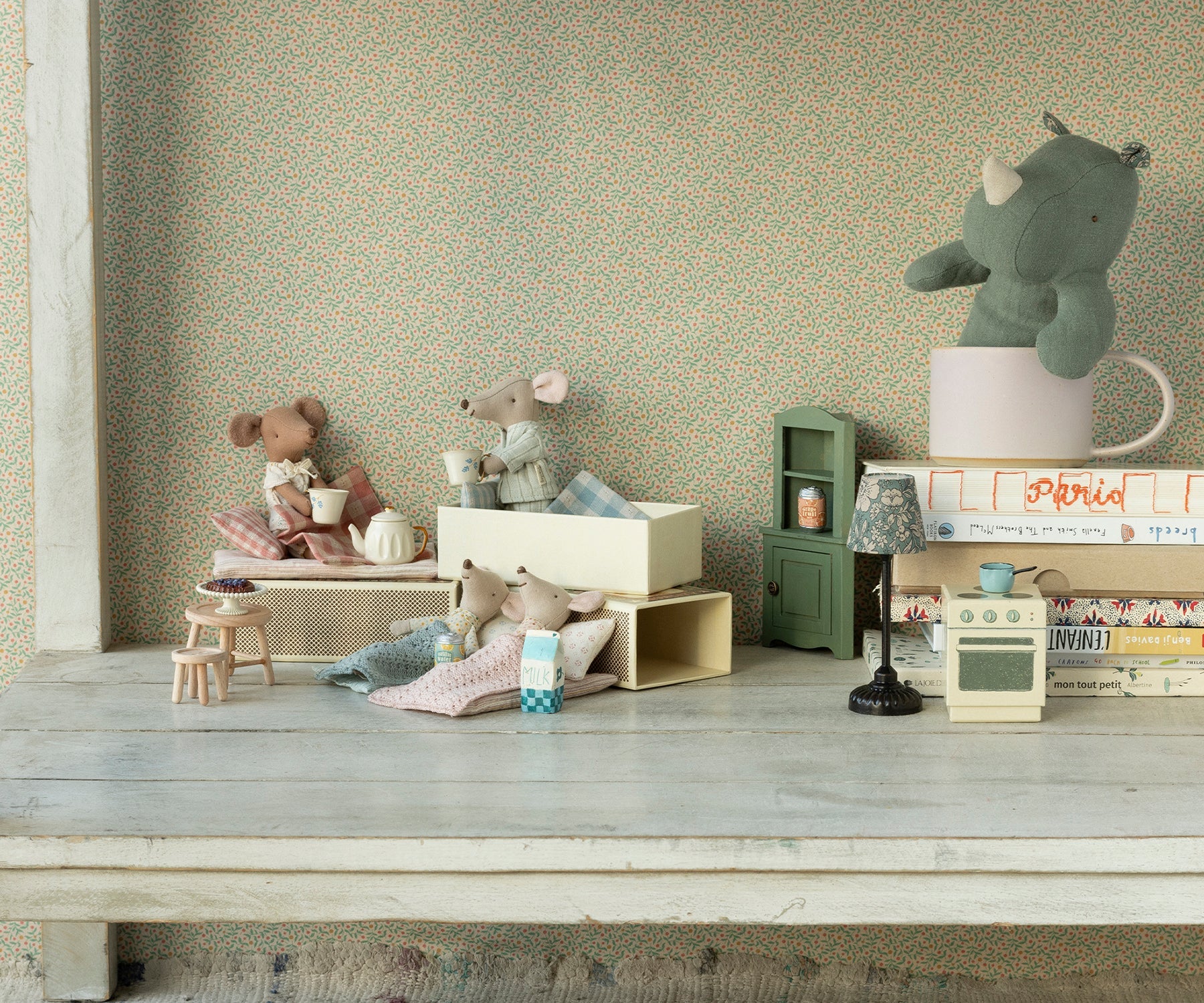 Miniature toys and furniture on a wooden surface with a patterned wall in the background.