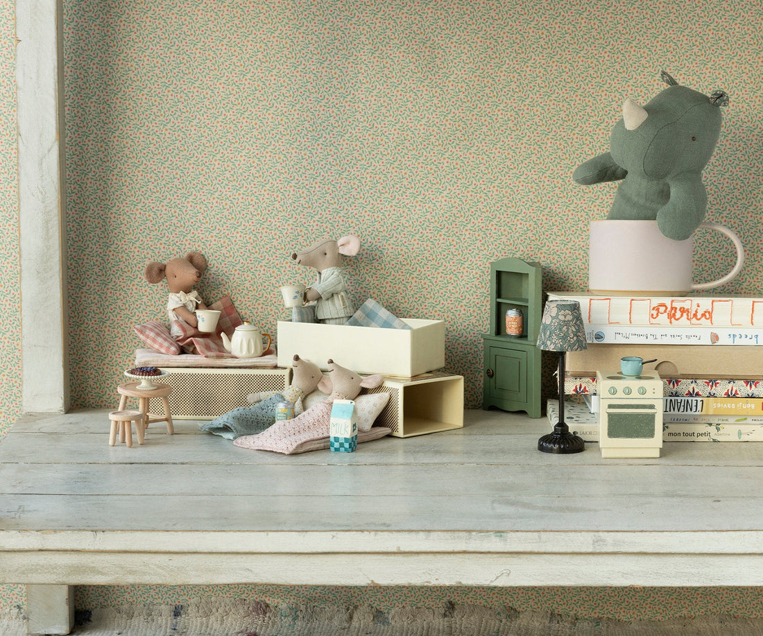Miniature toys and furniture on a wooden surface with a patterned wall in the background. 