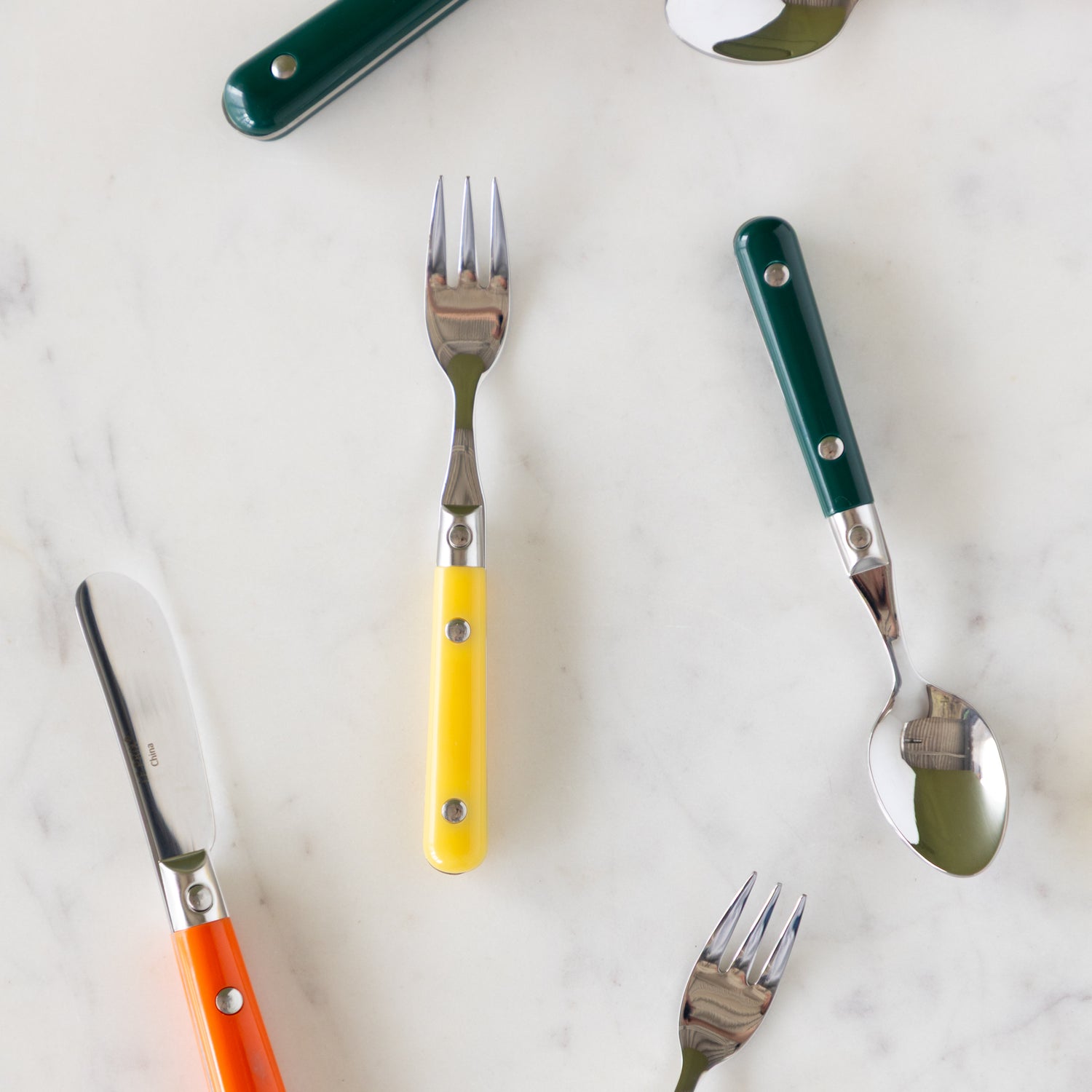 LePrix Cutlery utensils in dark green, orange and yellow scattered on a table.