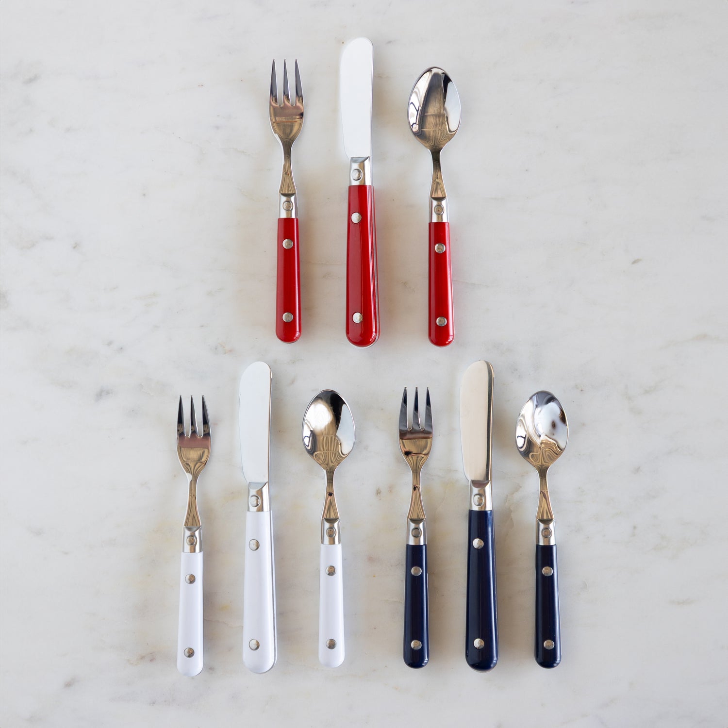 A set of flatware with red, white, and blue handles, including forks, knives, and spoons, displayed on a marble surface.