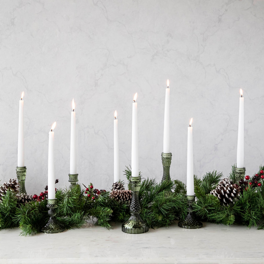 A collection of vintage green glass candlesticks with lit white candles on a table.