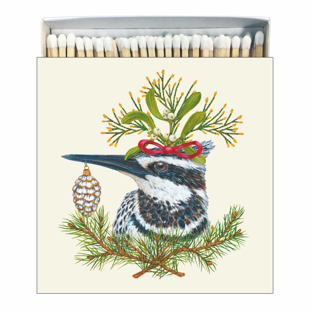 A square box of matches with a whimsical bird illustration surrounded by holiday greenery and decorations, artwork by Vicki Sawyer.