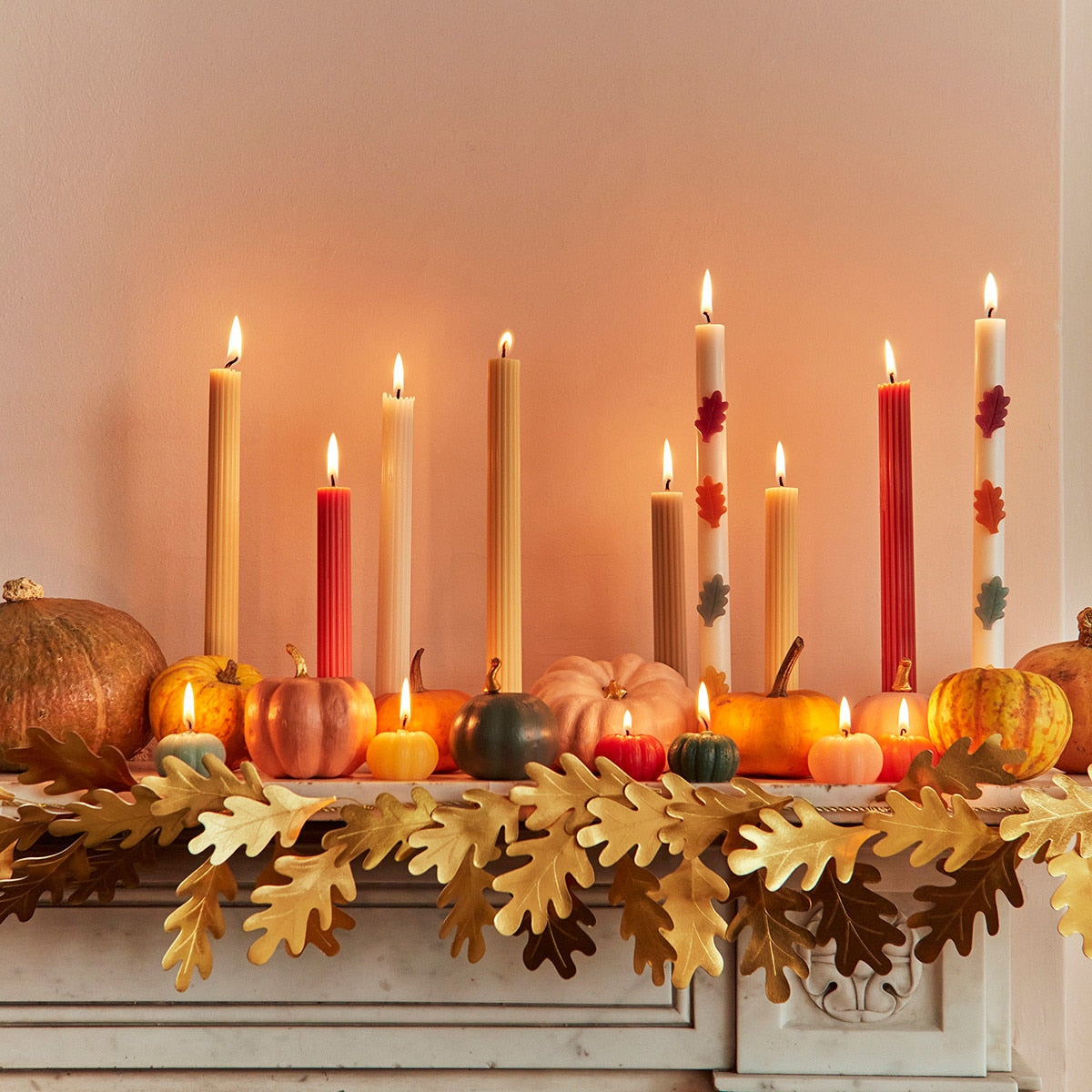 Decorative mantel with candles, pumpkins, and fall leaves on a neutral background.