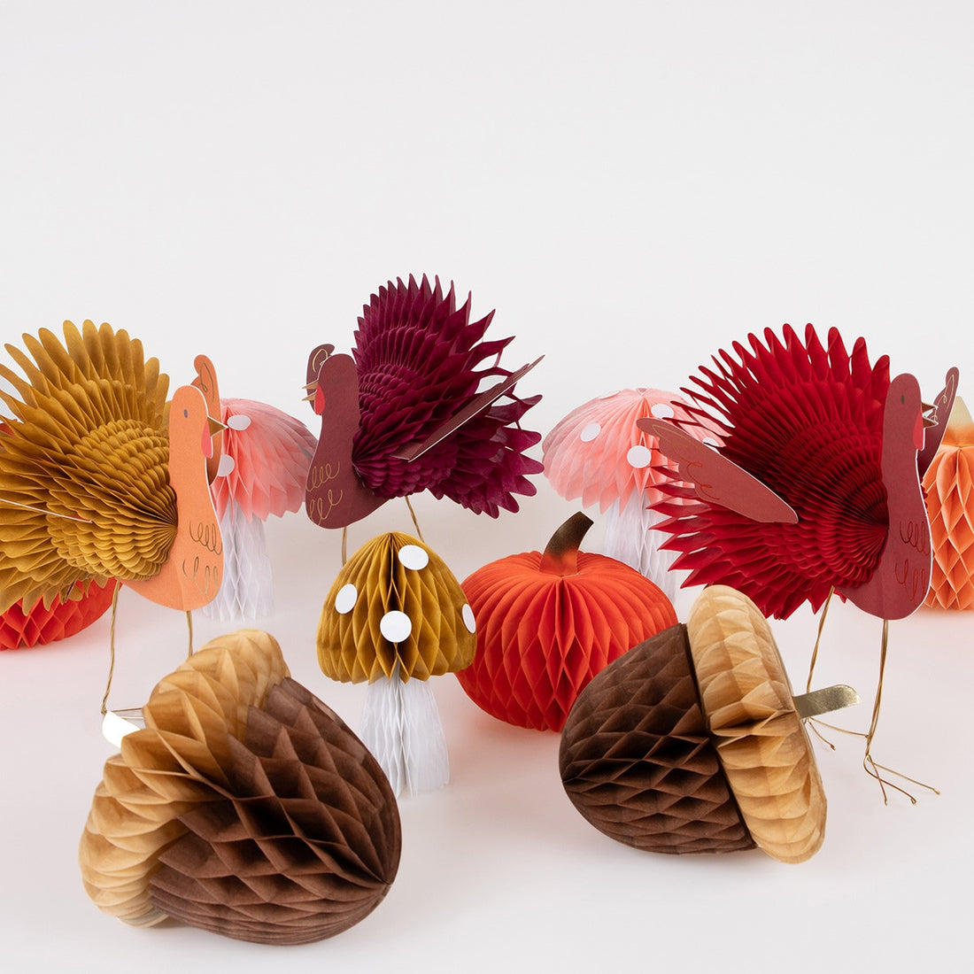 A variety of tissue paper honeycomb decorations with vintage designs including orange and peach pumpkins, mushrooms, acorns, and turkeys in shades of maroon and red.