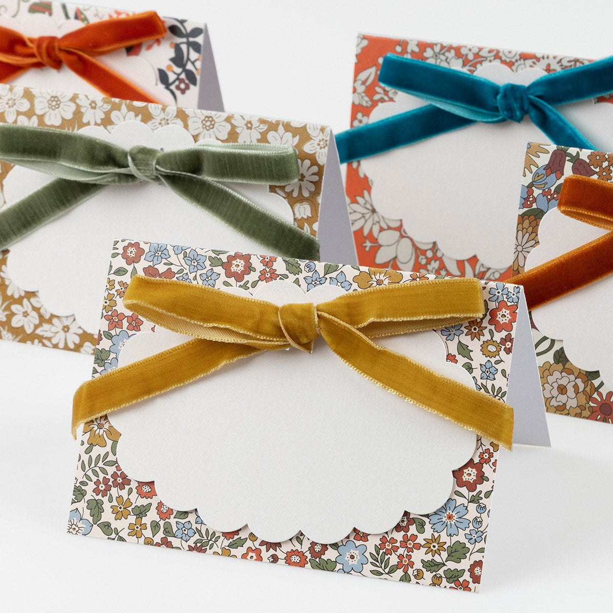 6 paper place cards featuring 6 different Liberty floral prints in warm fall colors.
Each is decorated with a luxurious velvet bow in burnt orange, muted gold, teal, sage, berry red or dusty pink with pale matte gold foil details. Each place card comes with a scalloped paper tag for you to write the name on.
