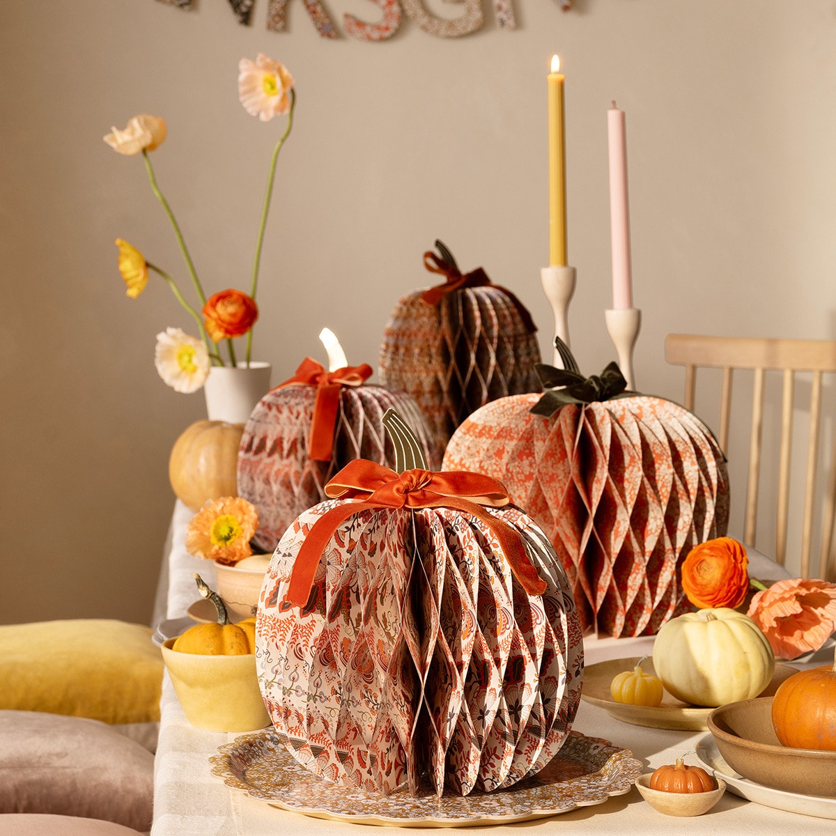 Decorative pumpkins with ribbons on a table with flowers and candles.