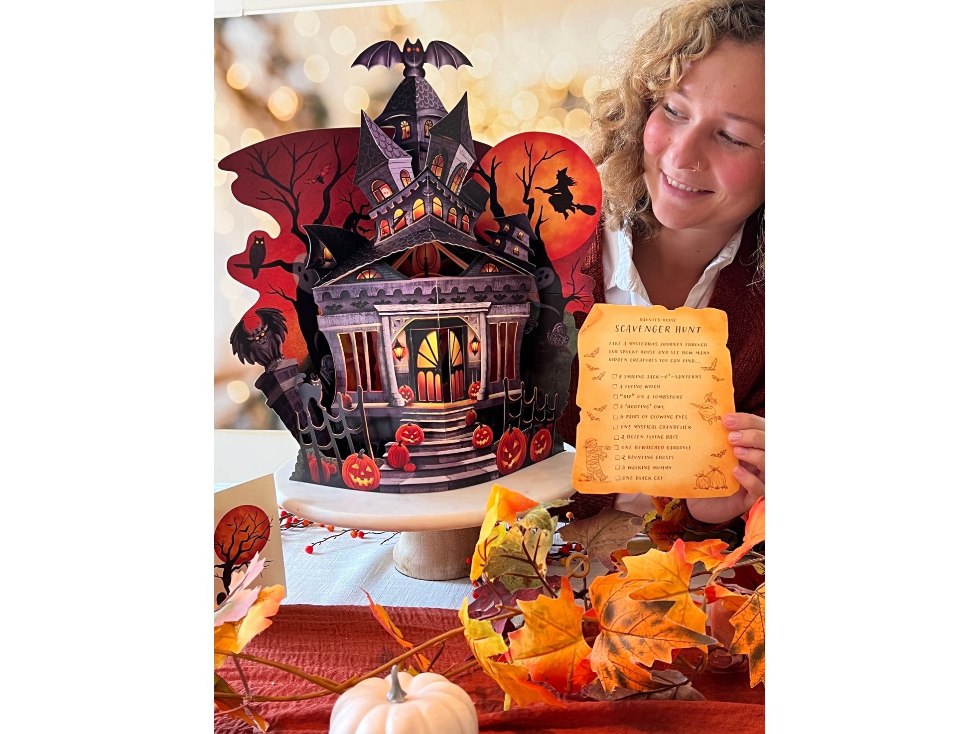 Woman holding a Halloween-themed pop-up card with a haunted house design.