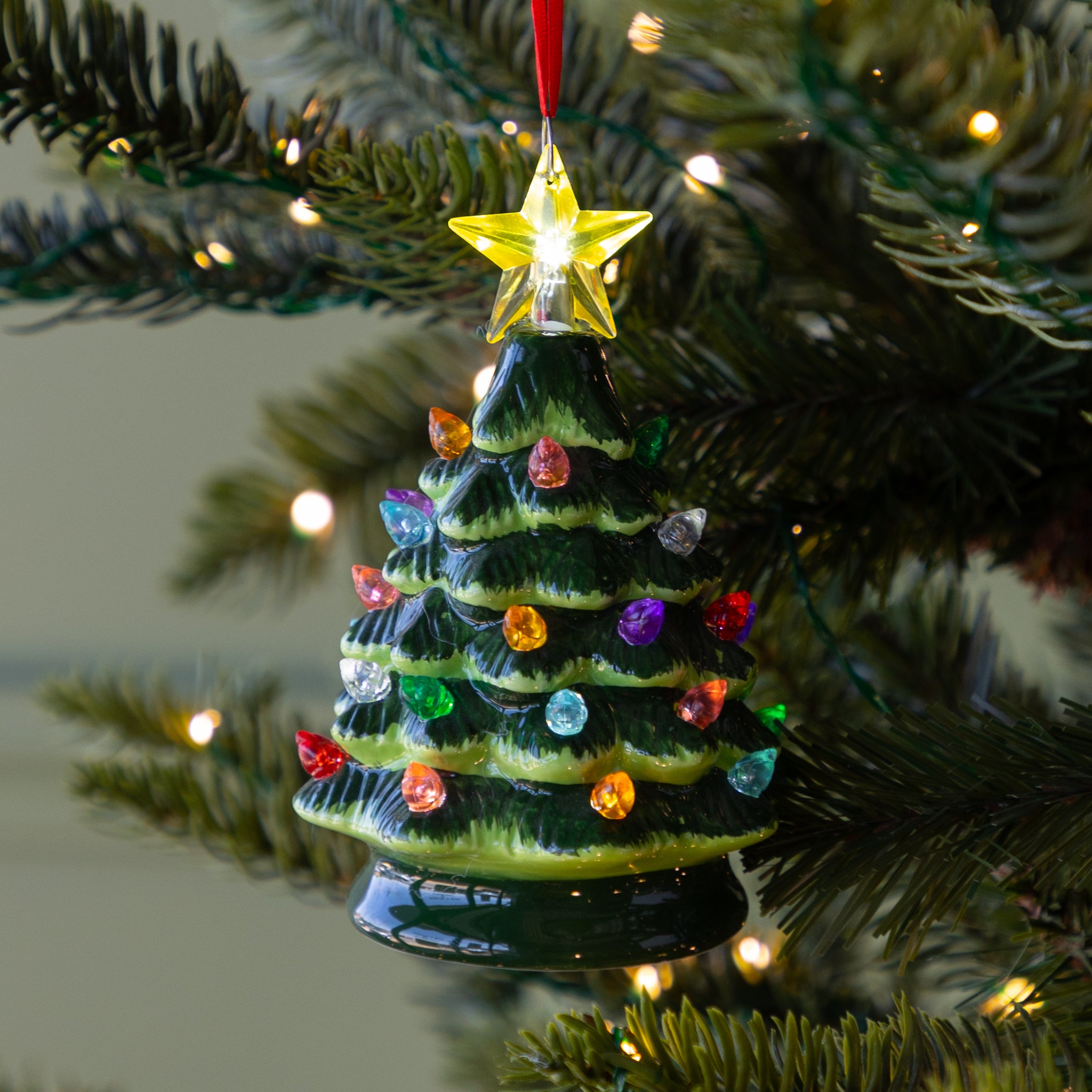 Vintage Lighted Christmas Tree Ornament featuring colorful lit bulbs and a lit yellow star on top, hanging on a lit Christmas tree.