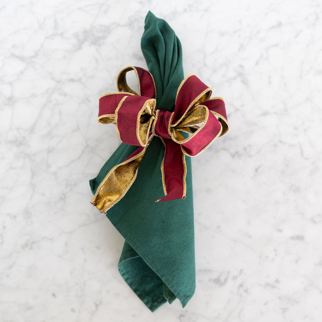 Green napkin with a red and gold bow on a textured white background.