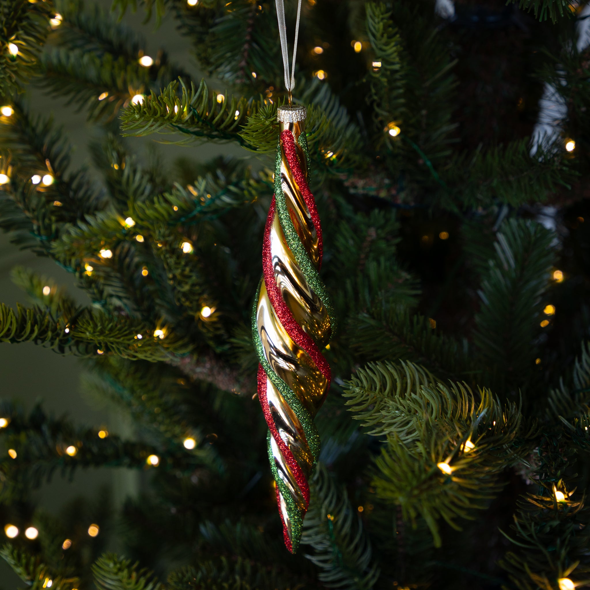 Red & Gold Twirl Ornament with a gold base and glittery red and green swirls on a lit Christmas tree.