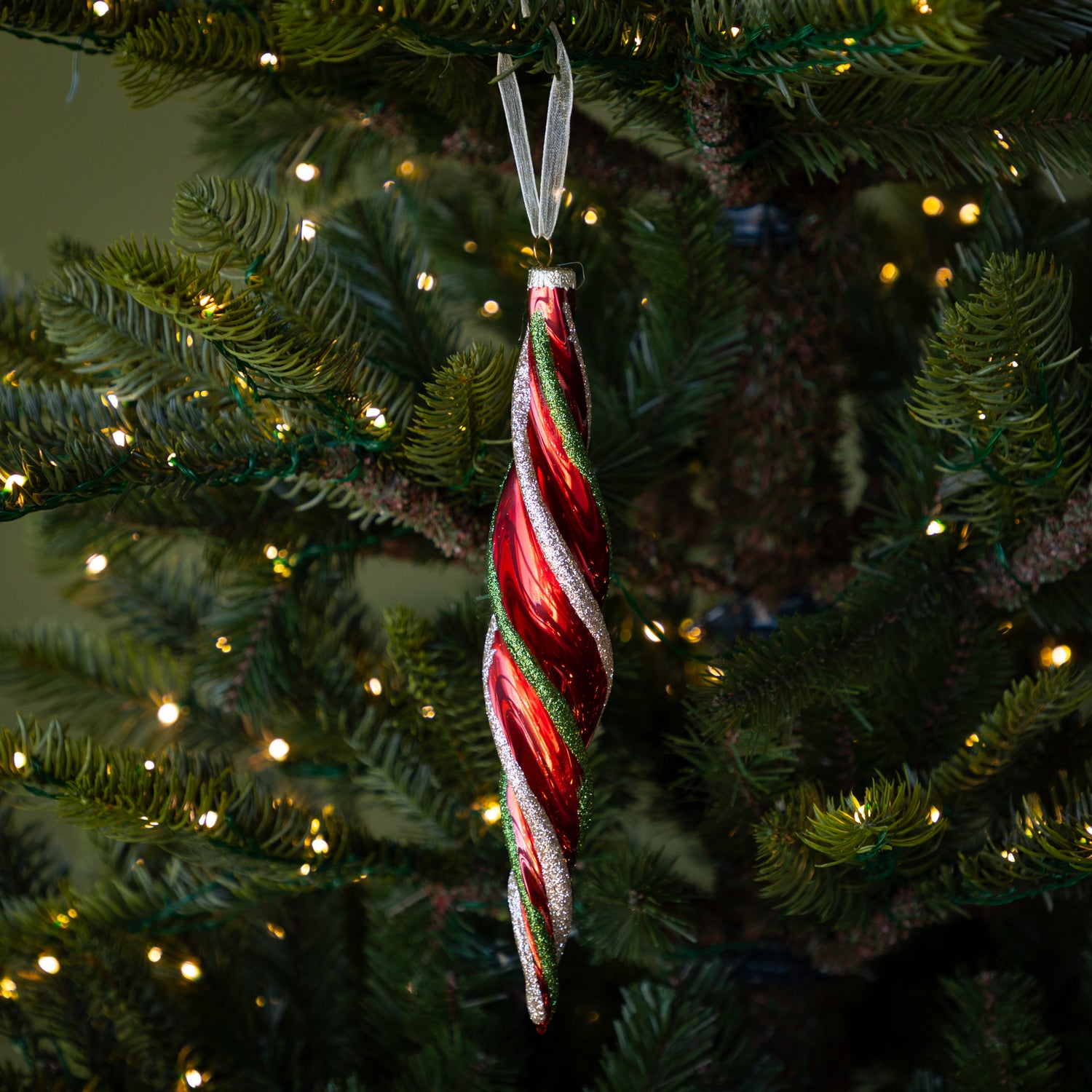 Red & Gold Twirl Ornament with a red base and glittery red and green swirls on a lit Christmas tree.
