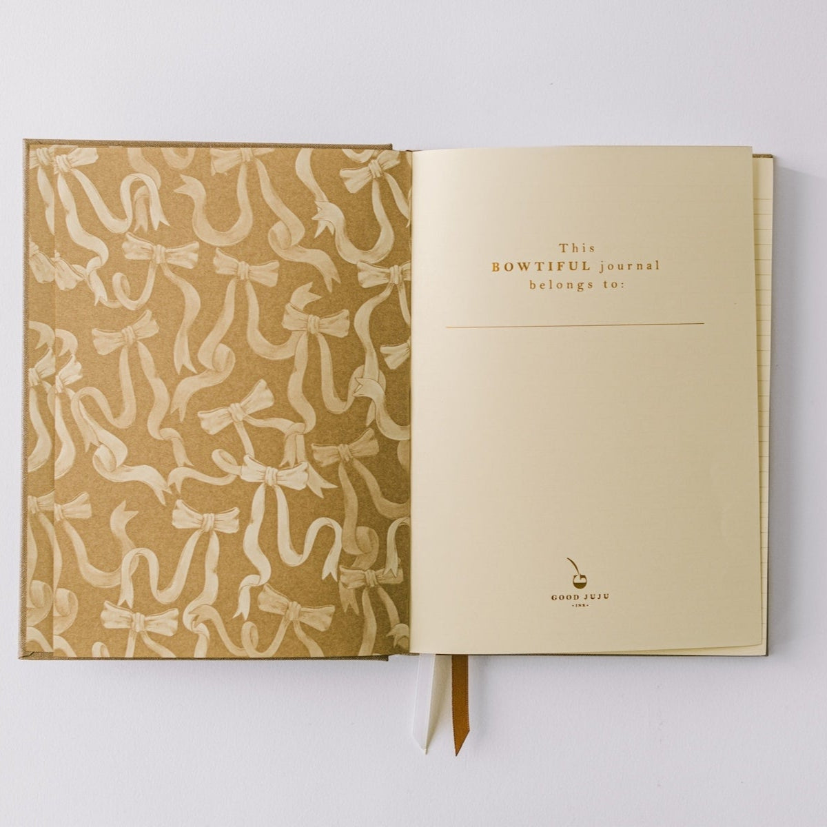 Notebook by Good Juju with gold detailing depicting a bow. 