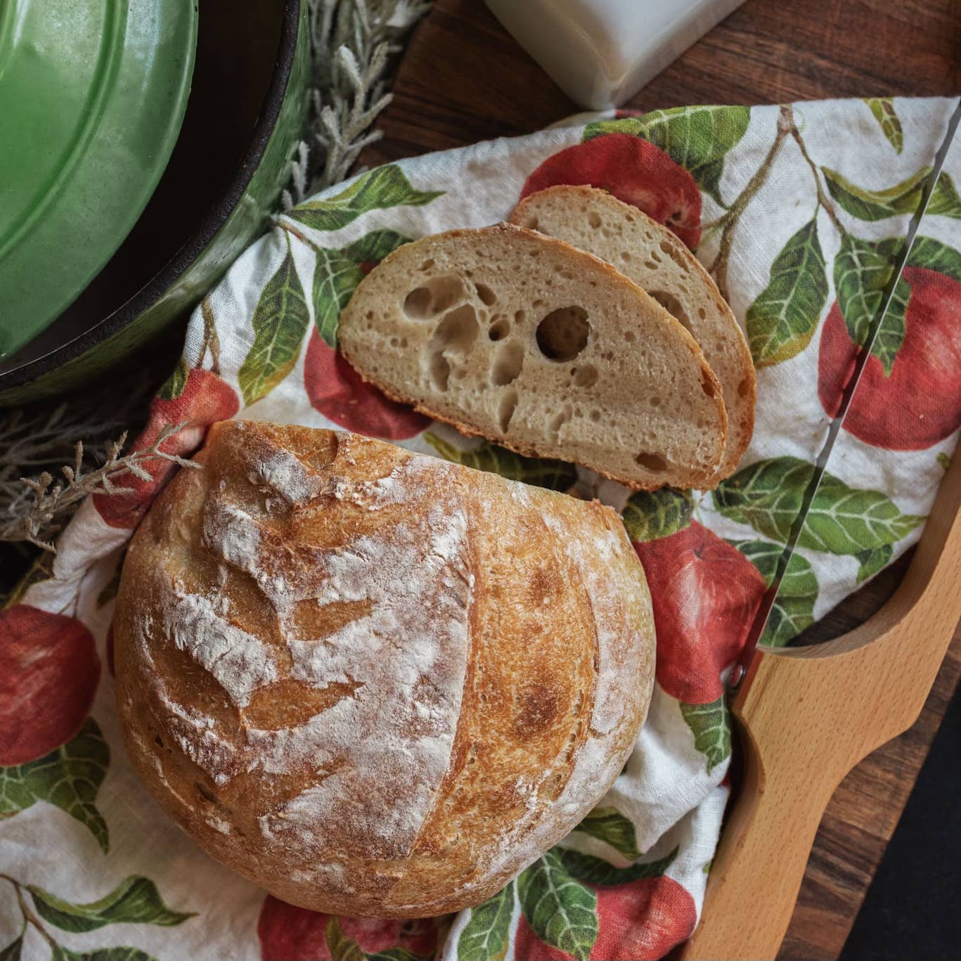 Loaf of bread with slices on a decorative cloth with apples and leaves