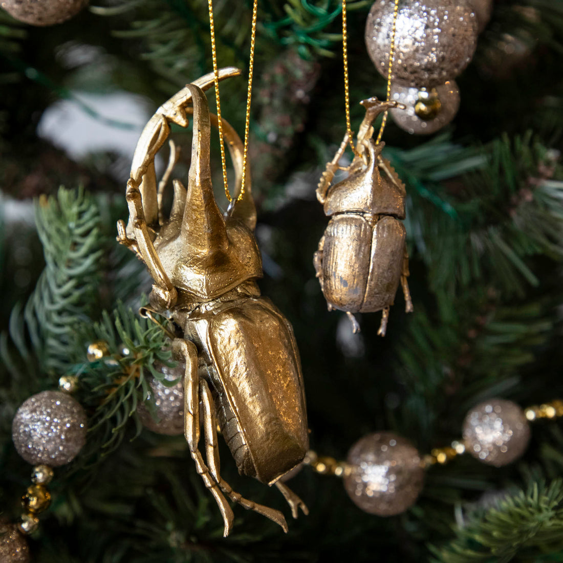 Gold-colored metal beetle-shaped ornaments hanging on a Christmas tree.