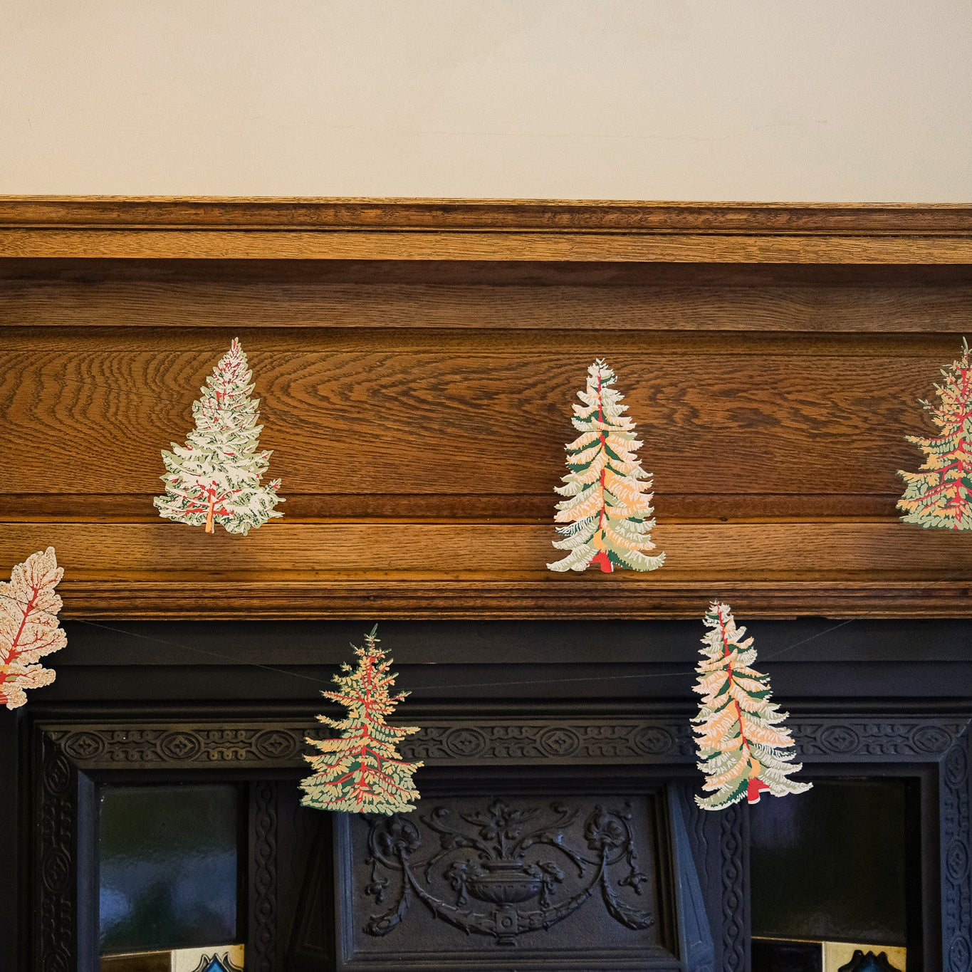 Decorative Christmas trees on a wooden mantelpiece with a fireplace in the background.