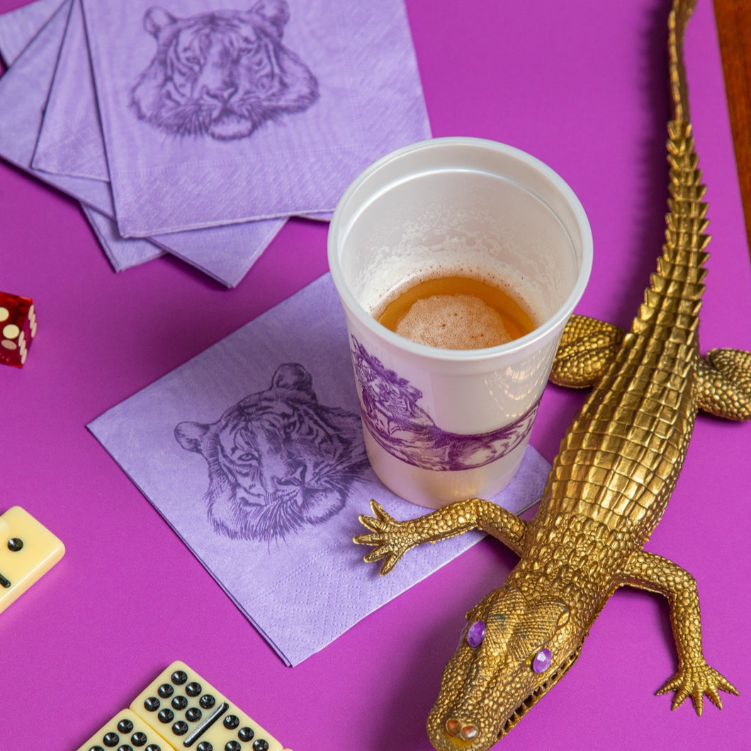 Gold alligator, dominoes, and a cup with a drink along with the Tiger Beverage Napkin on a table.
