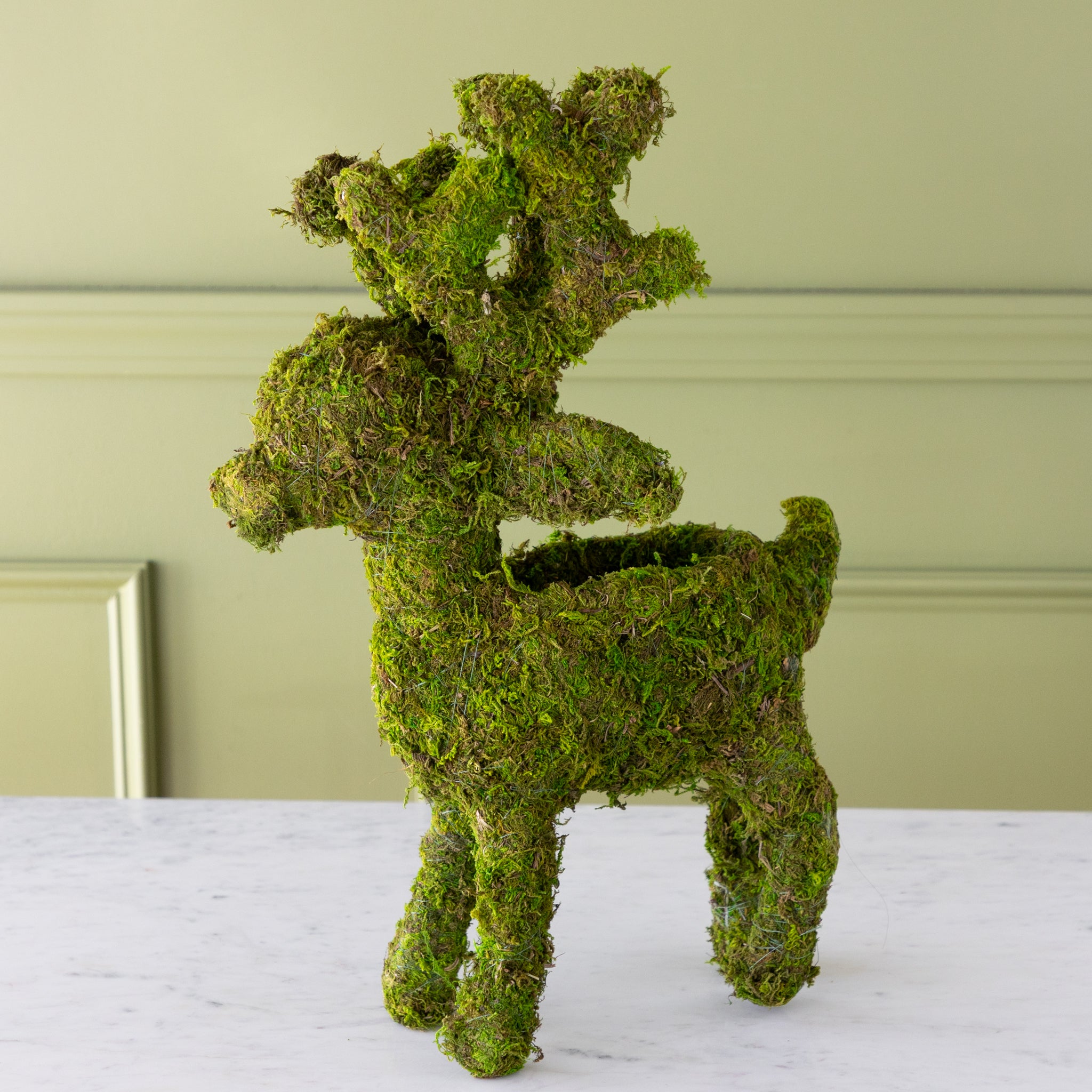 Moss-covered deer planter on a marble table with a light green wall background.