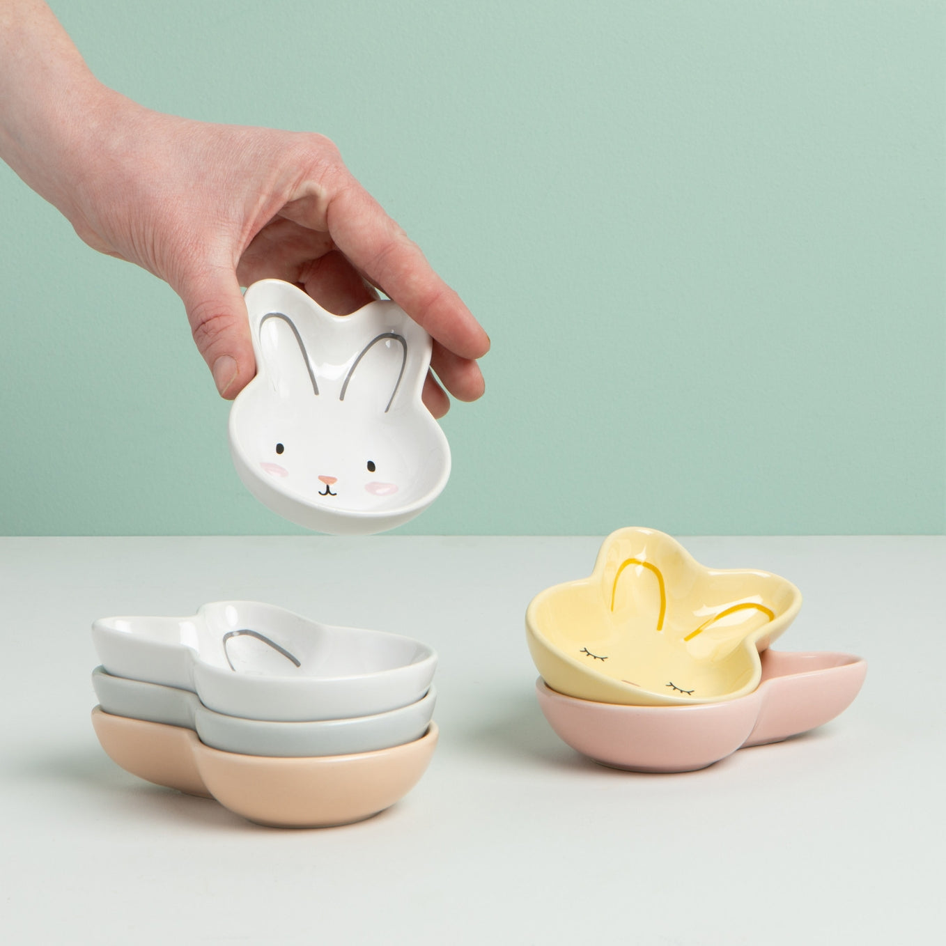 Small ceramic bowls with bunny faces on a light green background.
