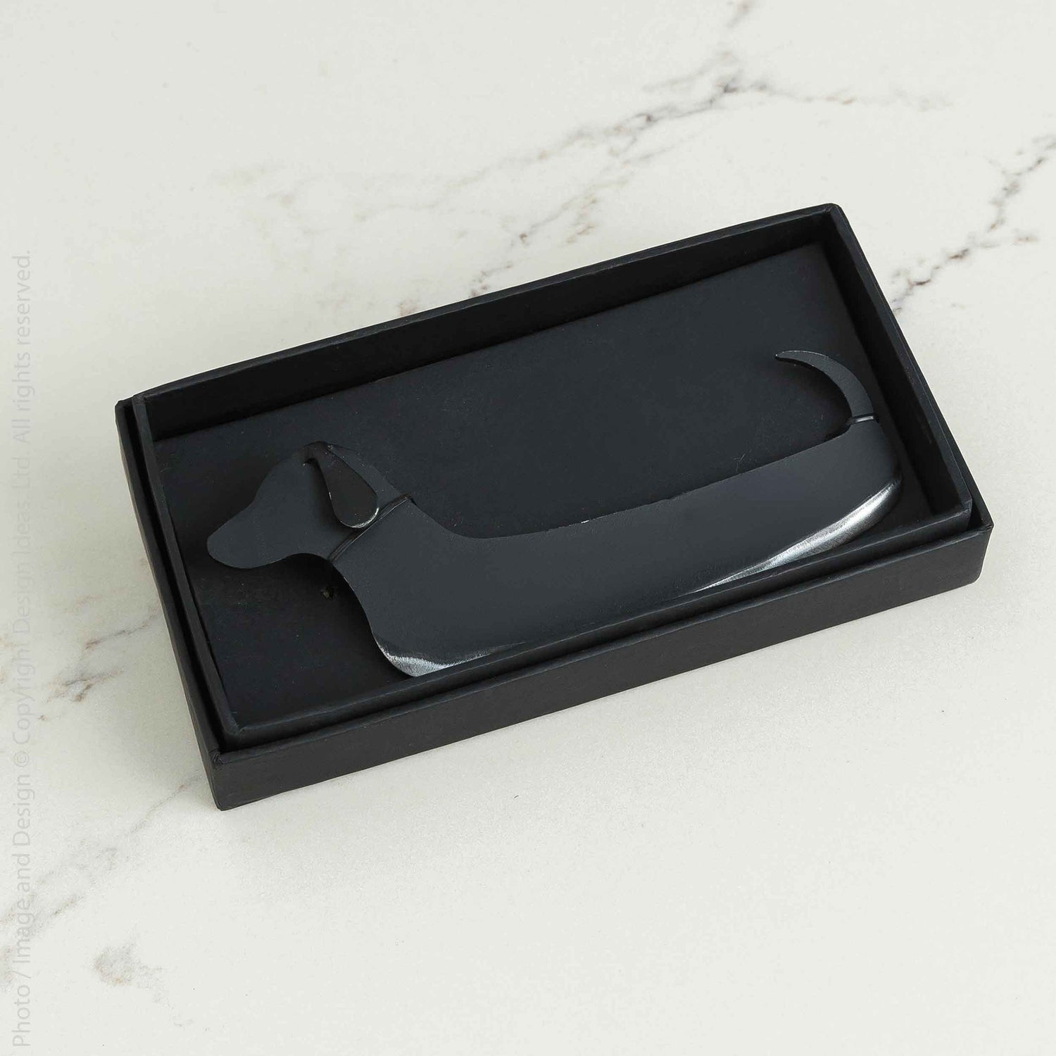 Black dog-shaped cheese knife in a black box on a marble surface