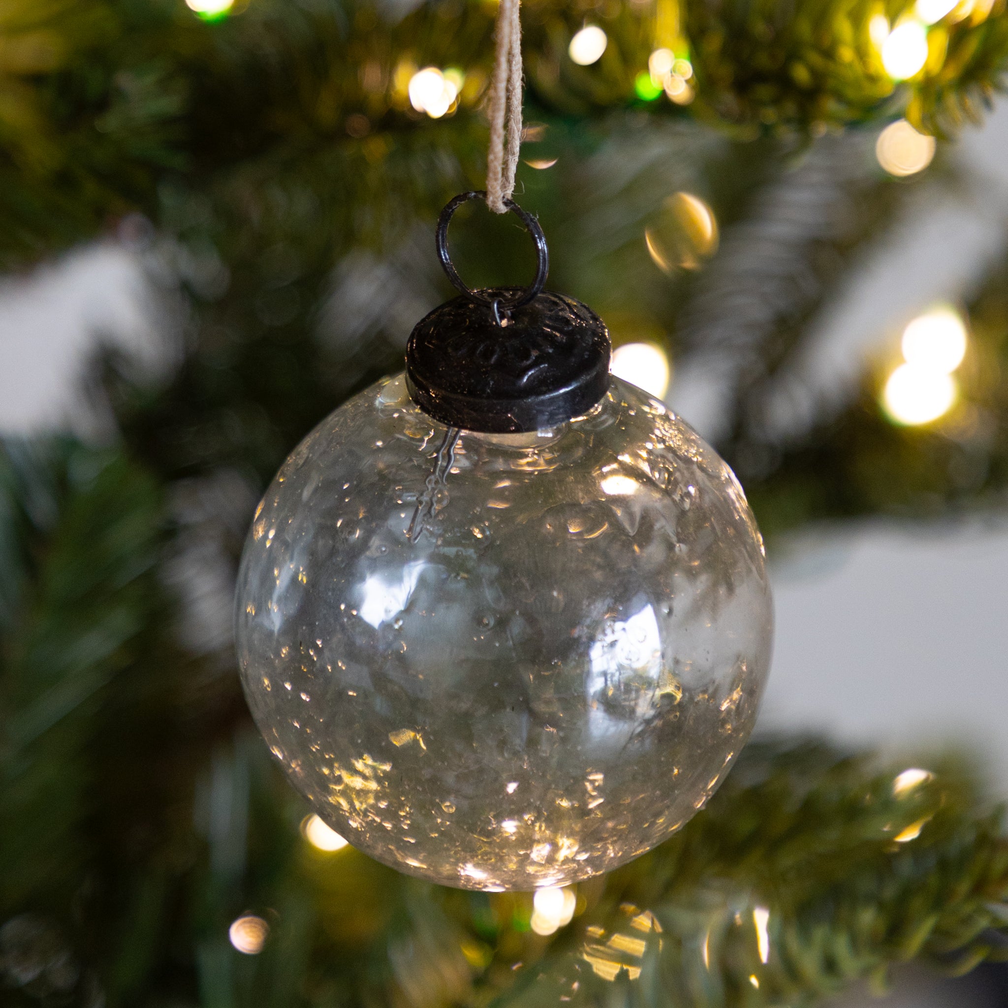 Clear glass ornament with black top hanging on a Christmas tree.