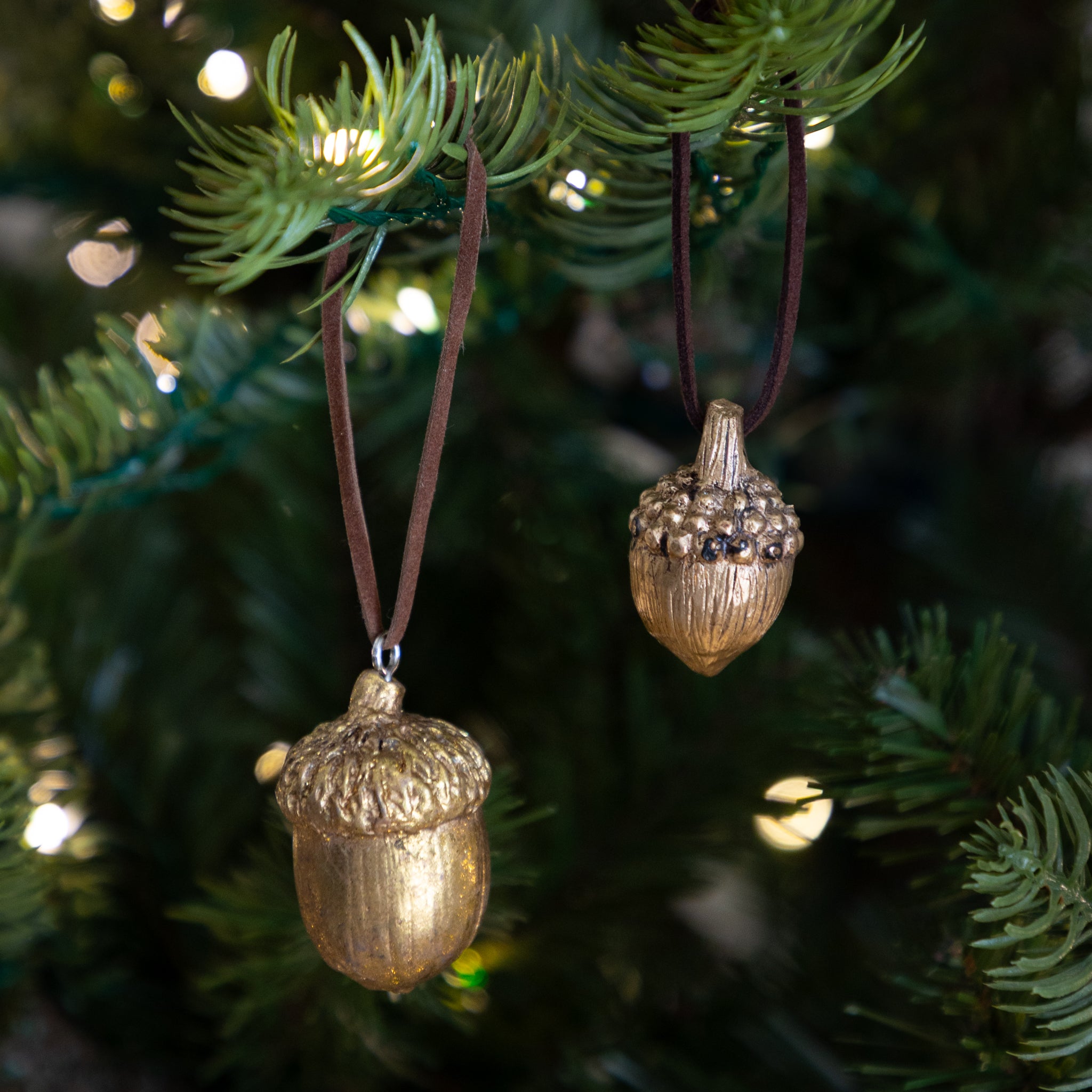 Two gold acorn-shaped ornaments hanging on a Christmas tree.
