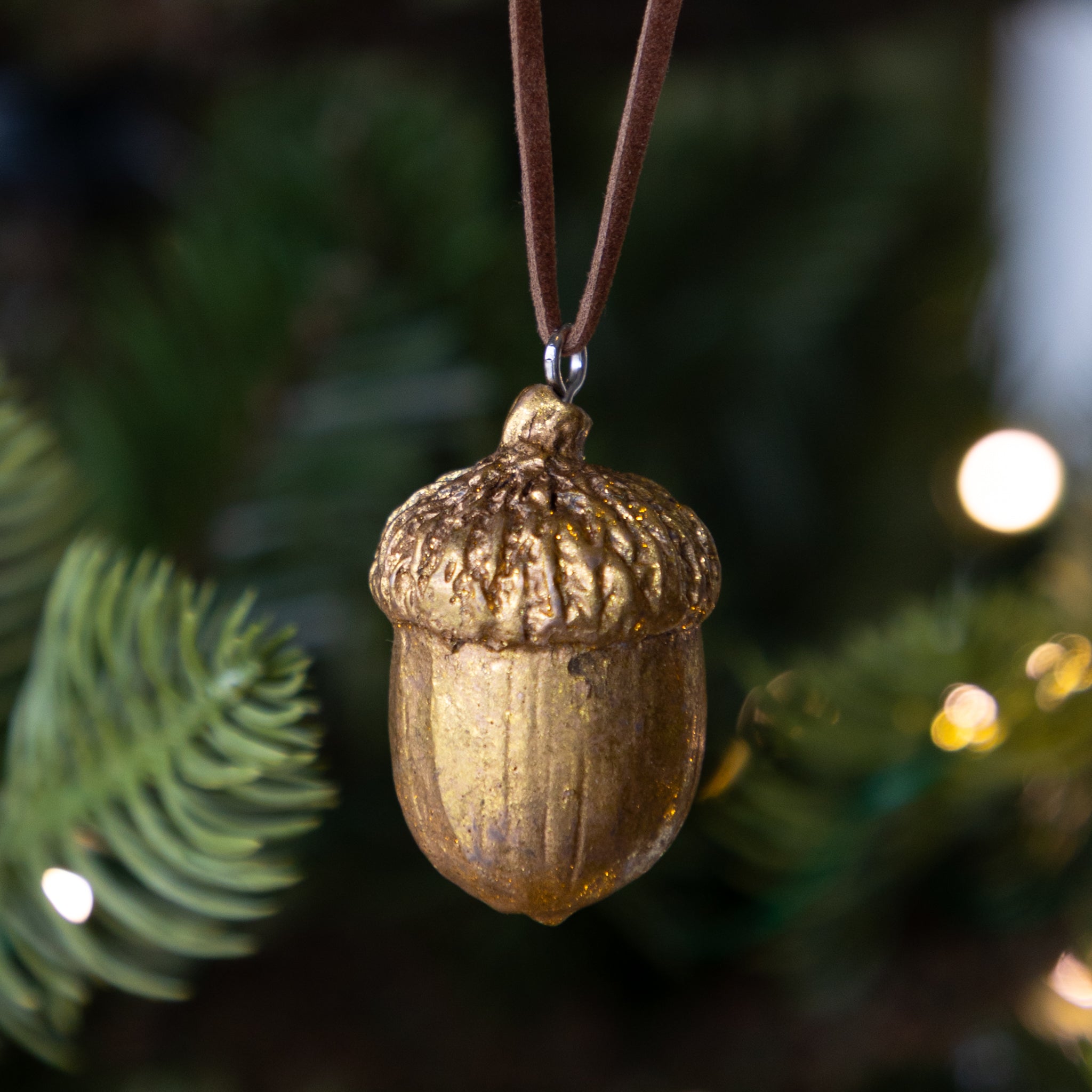 Gold acorn ornament hanging on a tree with blurred lights in the background.