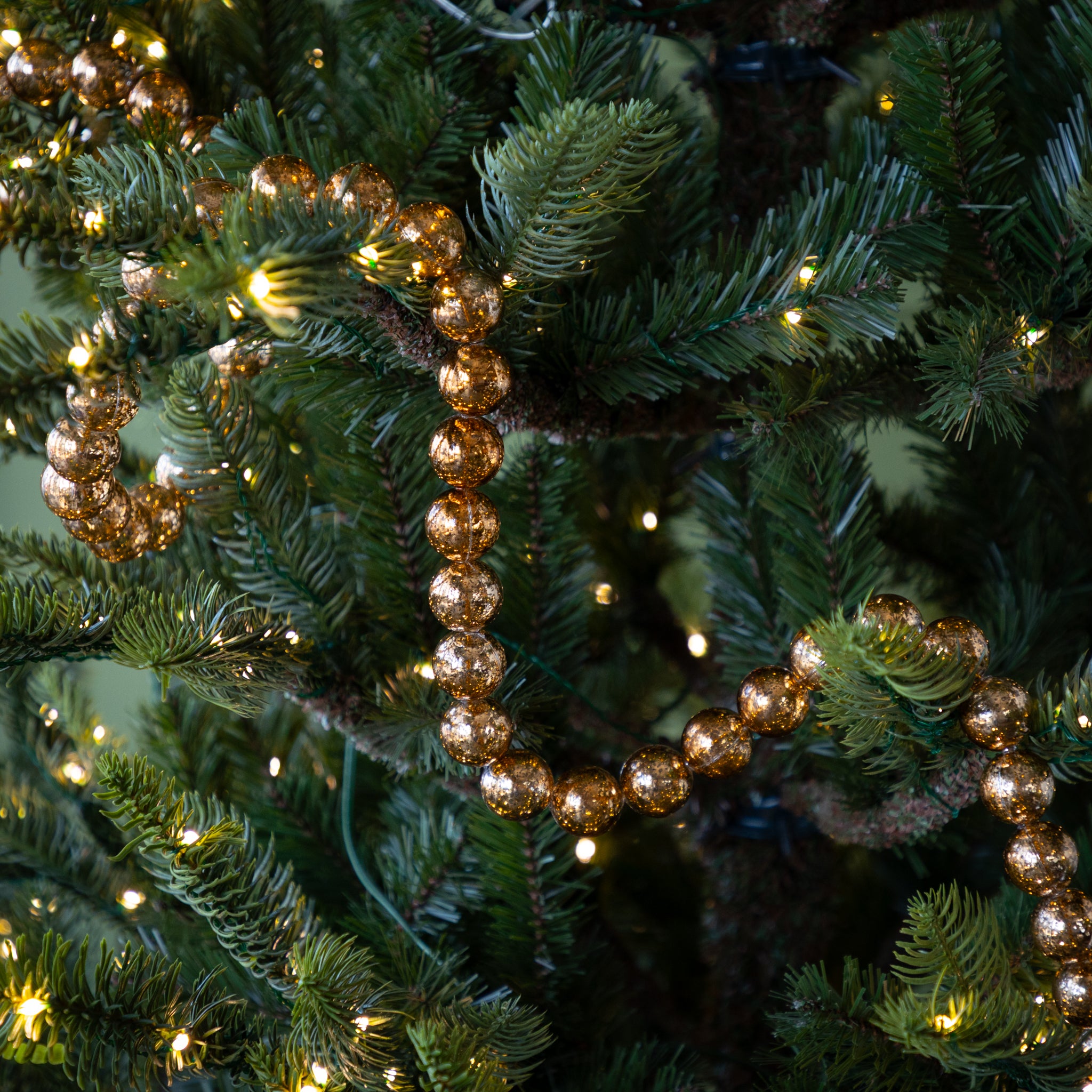 Decorative gold bead garland on a Christmas tree with lights.