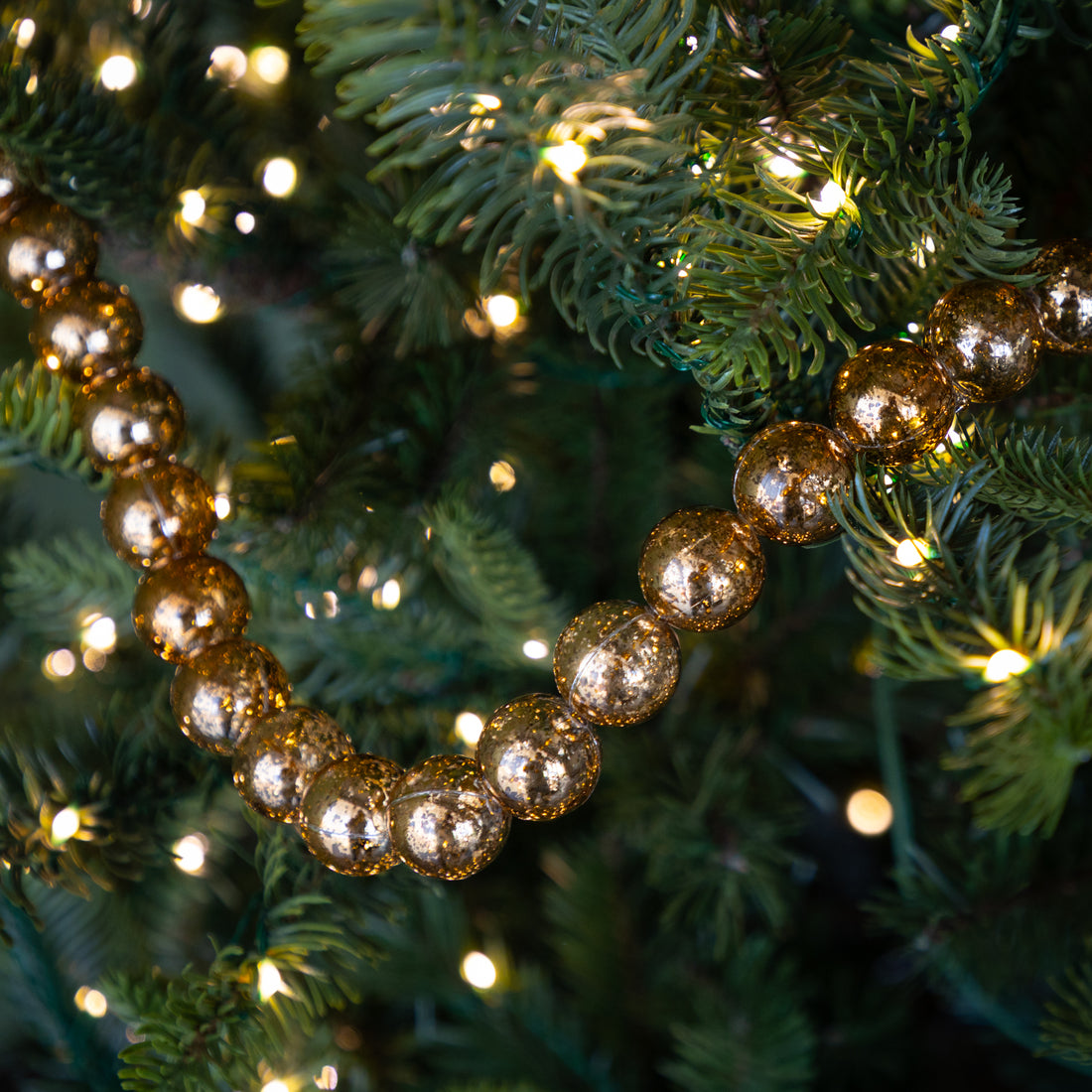 Decorative gold beaded garland on a Christmas tree with lights.