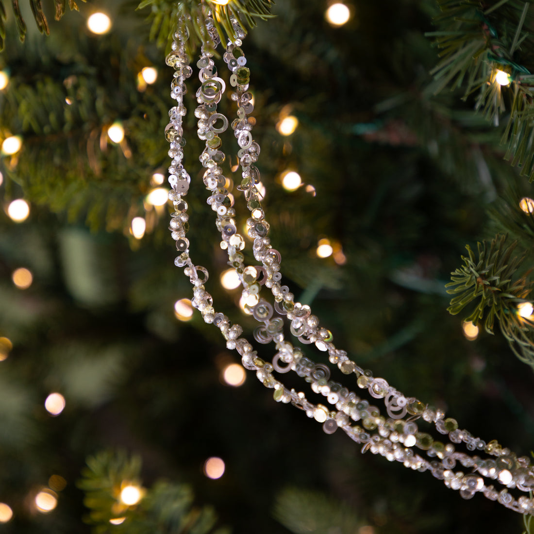 Decorative Three Strand Sequin Garland on a Christmas tree with blurred lights in the background.