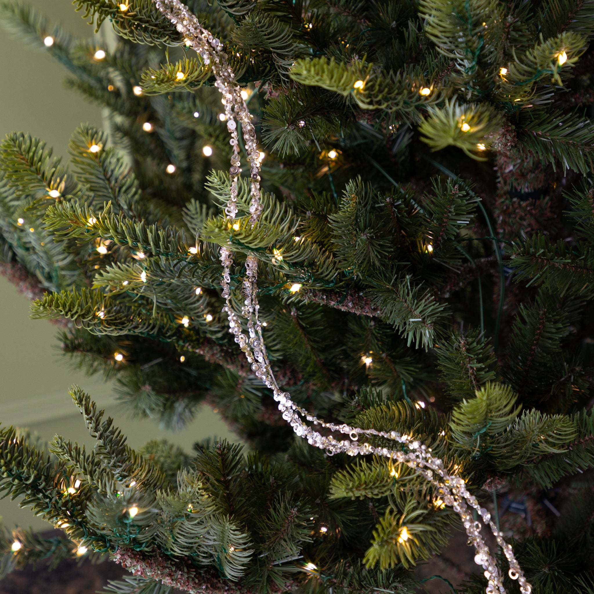 Decorative Three Strand Sequin Garland on a Christmas tree with blurred lights in the background.