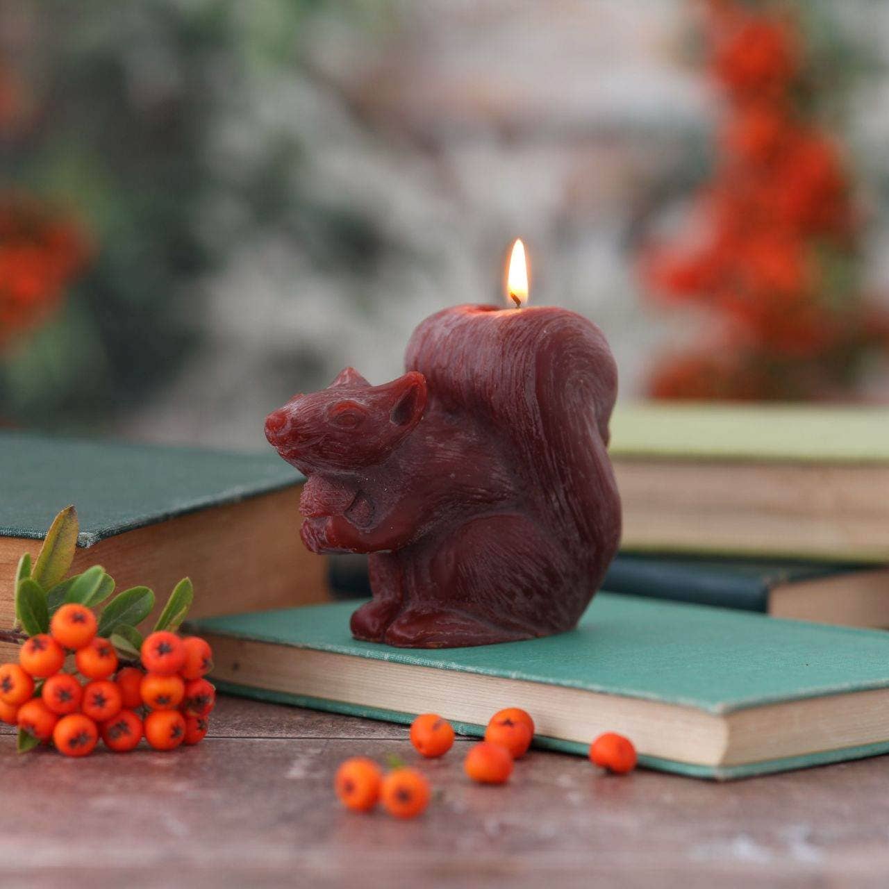Squirrel-shaped candle on a book with berries and a blurred natural background