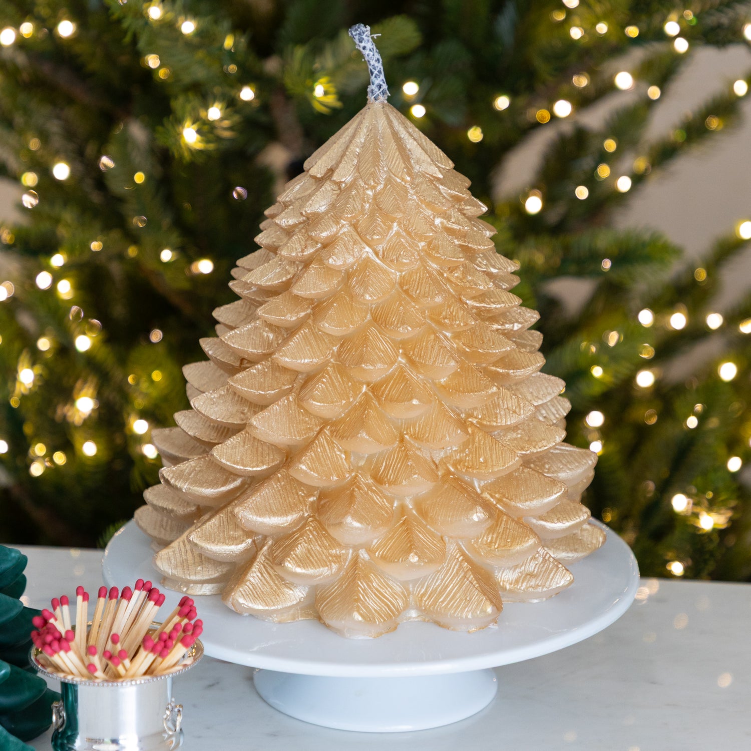 Gold candle shaped like a Christmas tree with blurred lights in the background.