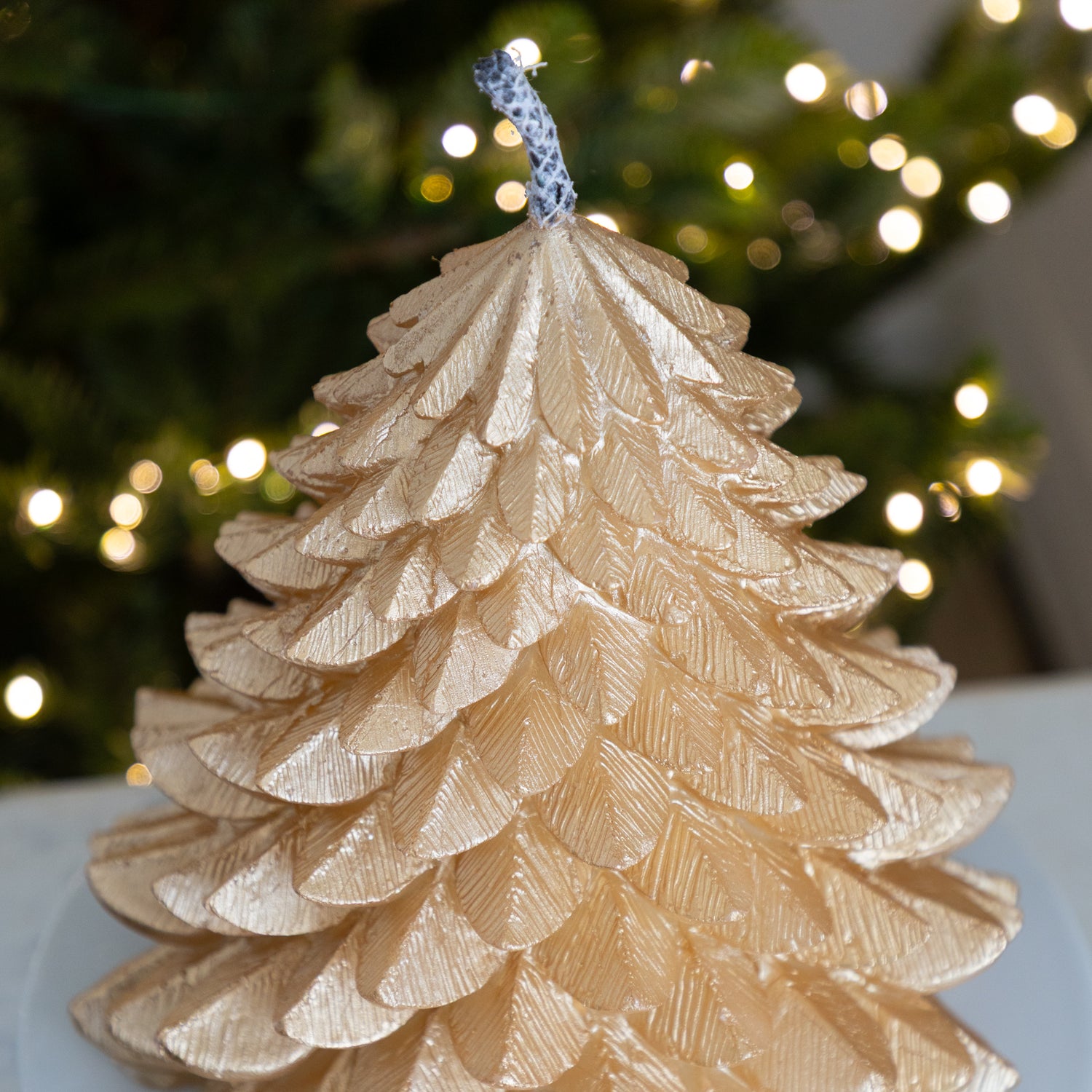 Green candle shaped like a Christmas tree with blurred lights in the background.
