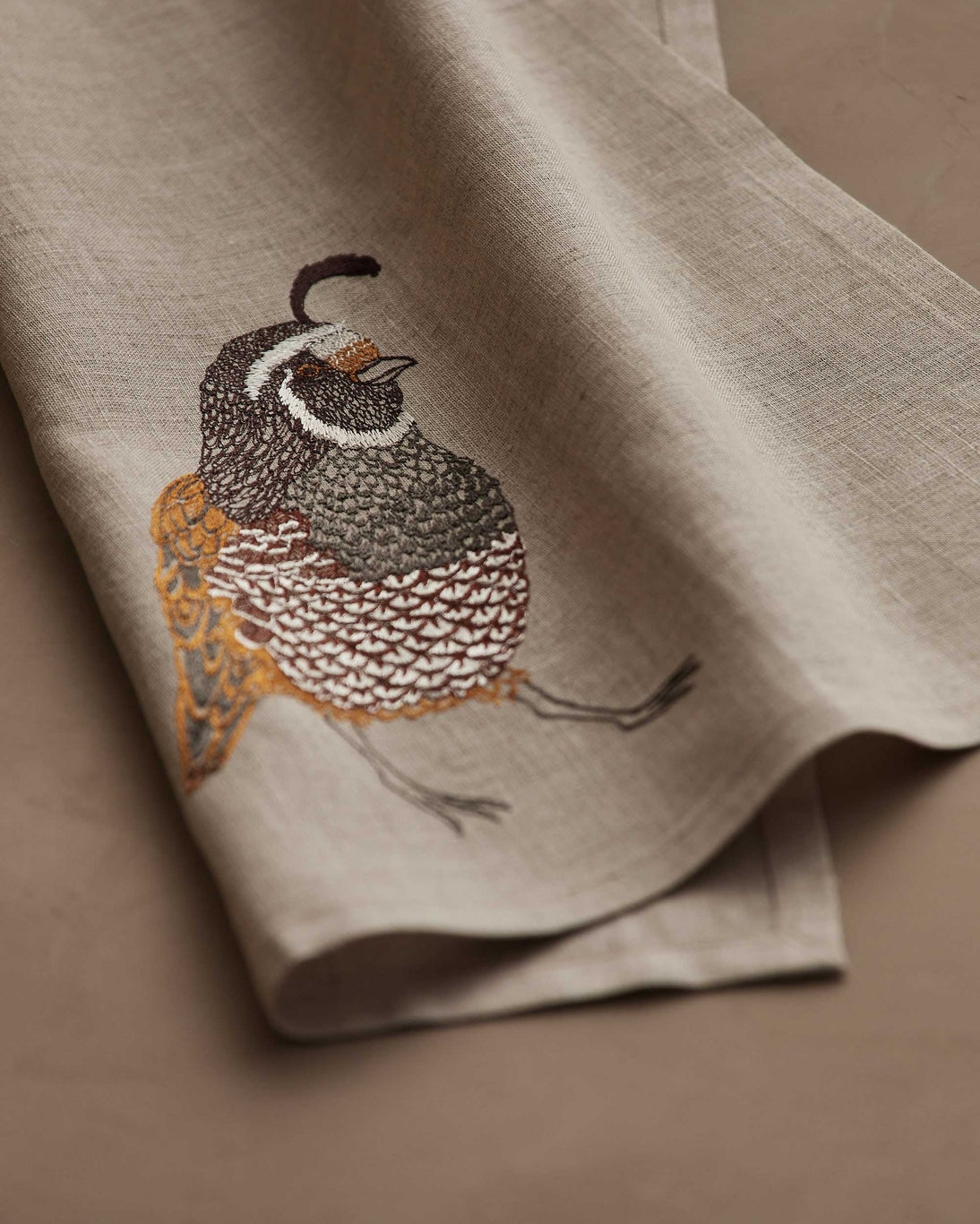 Embroidered quail design on a beige fabric background