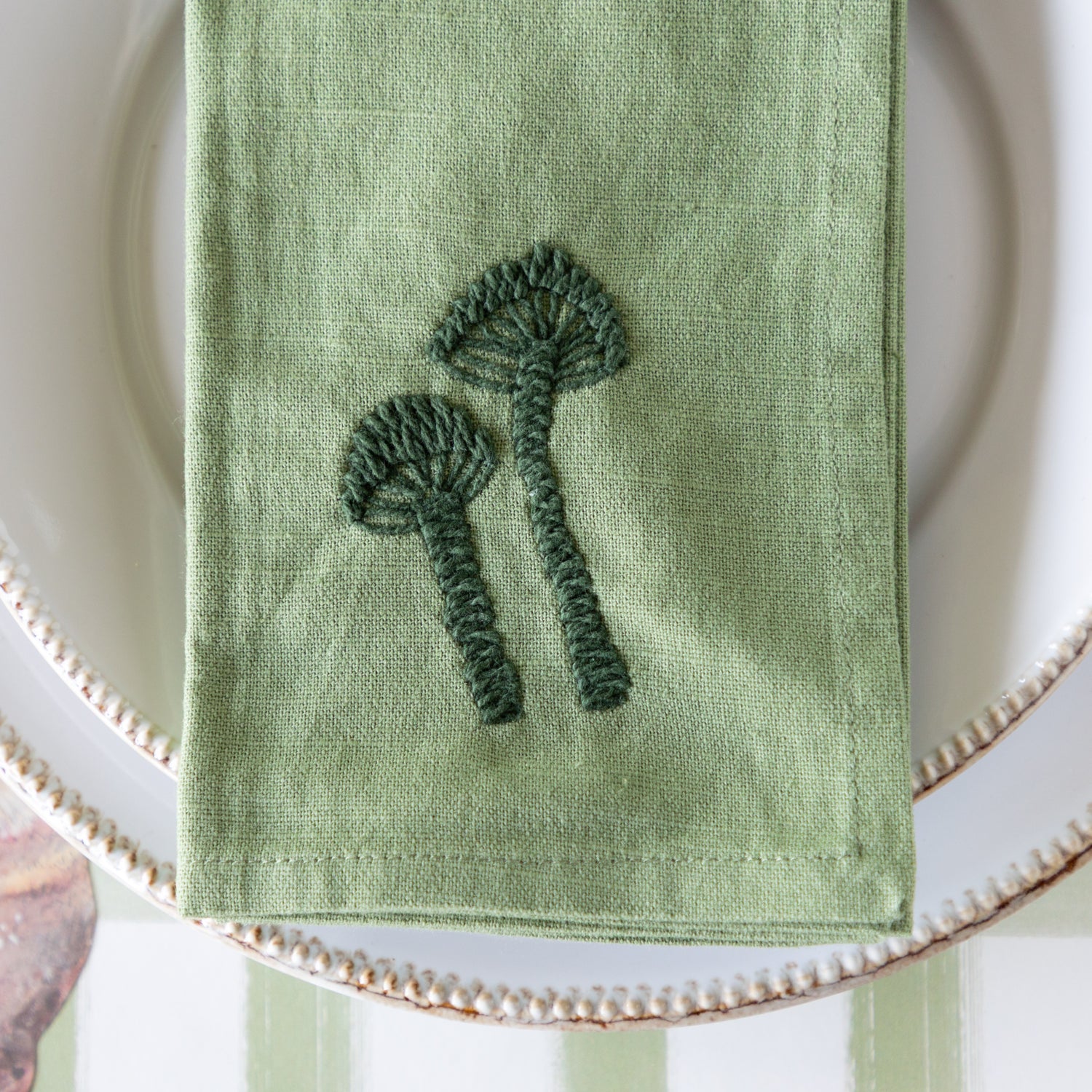 Green embroidered mushroom napkin on a white plate.