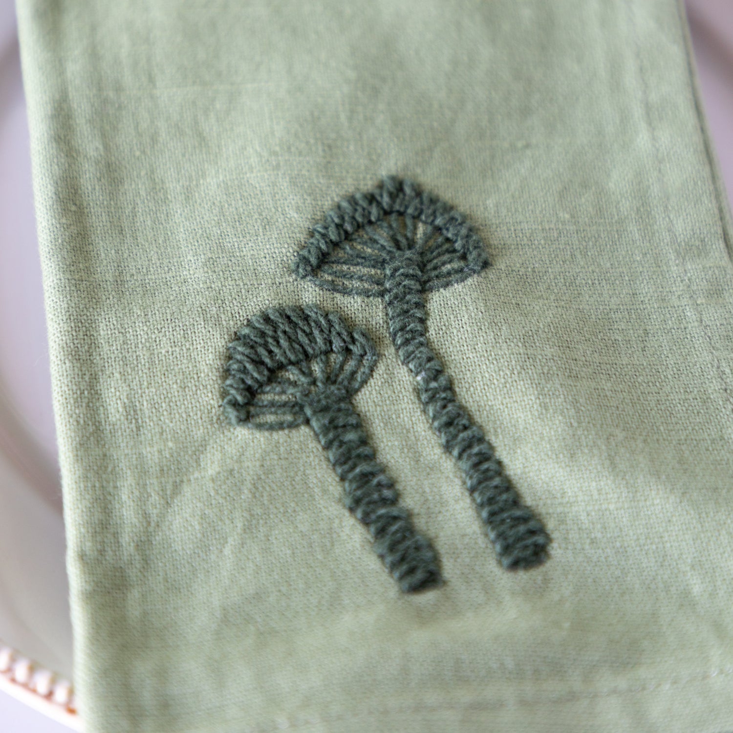 Green cloth napkin with embroidered dark green mushrooms.